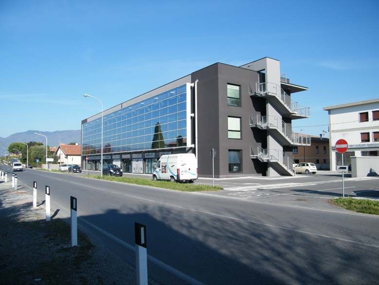 Moderno edificio commerciale con facciata in vetro, lato grigio scuro, scala esterna, su una strada soleggiata.