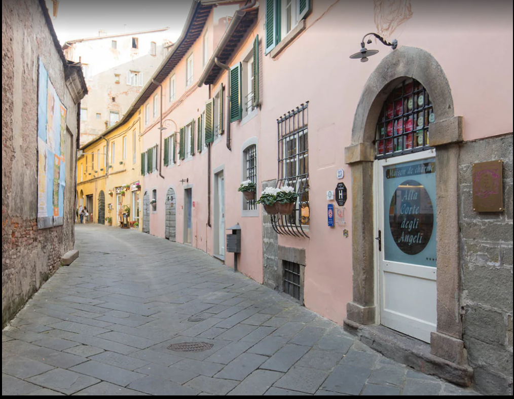 Strada acciottolata fiancheggiata da edifici color pastello, uno dei quali ha un portone con la scritta 