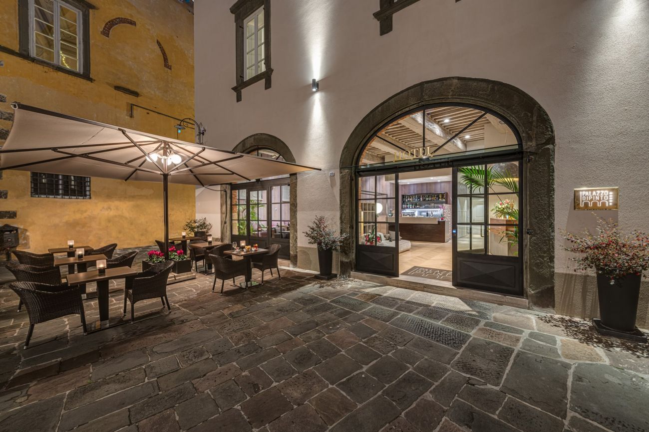 Esterno del ristorante di notte, con posti a sedere all'aperto sotto gli ombrelloni, porta ad arco e pavimento in ciottoli.
