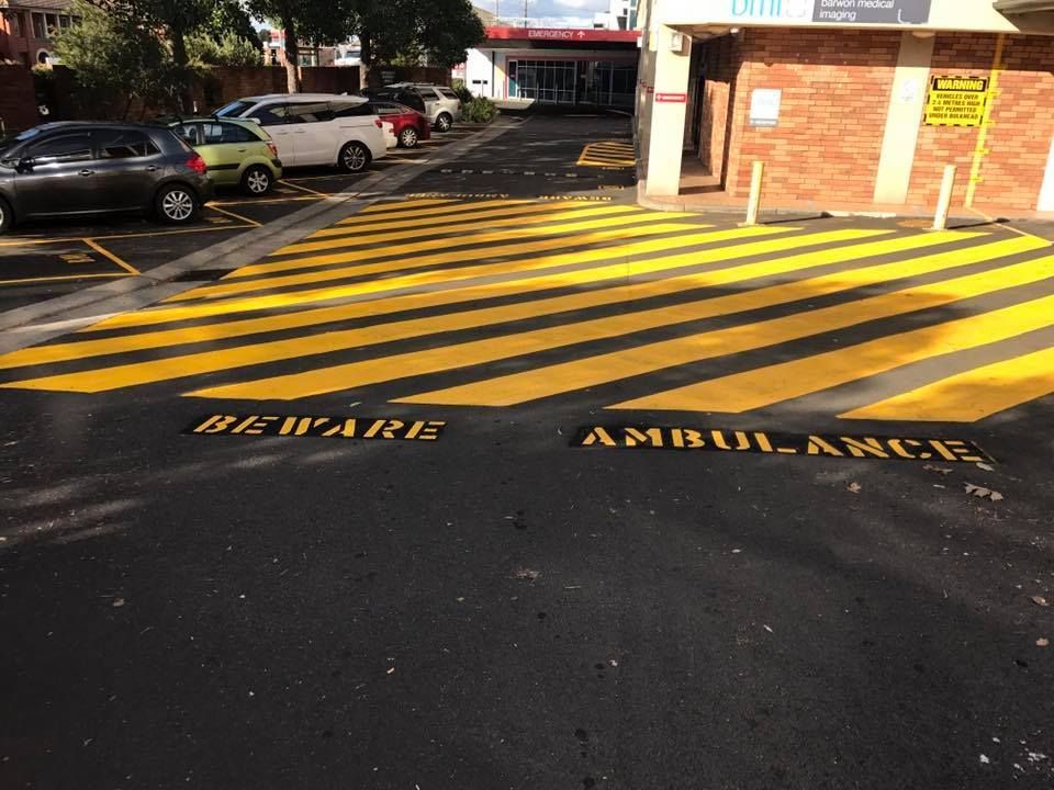 A yellow and black striped road with the words beware ambulance painted on it