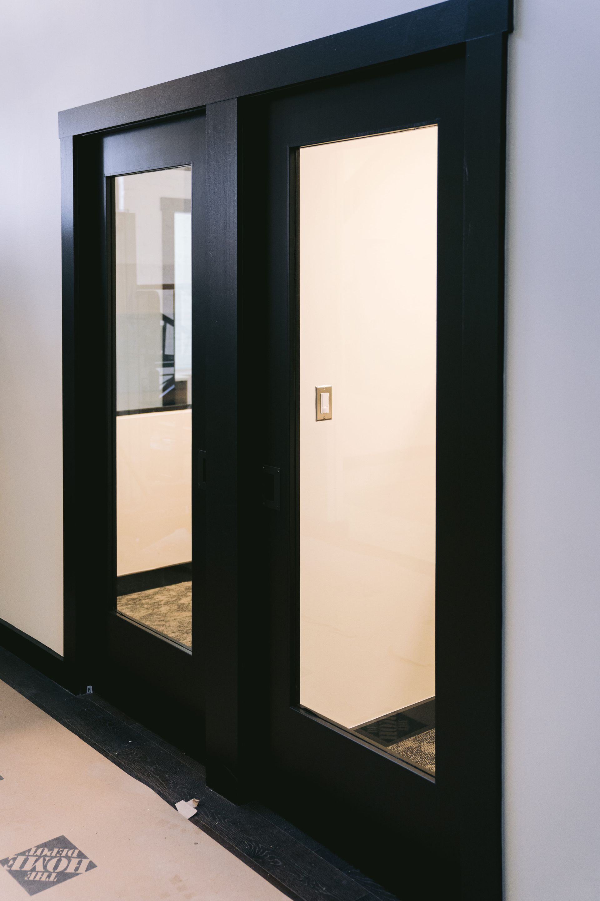 Black-framed glass double doors in a hallway, one door partly open, with beige walls and tile floor