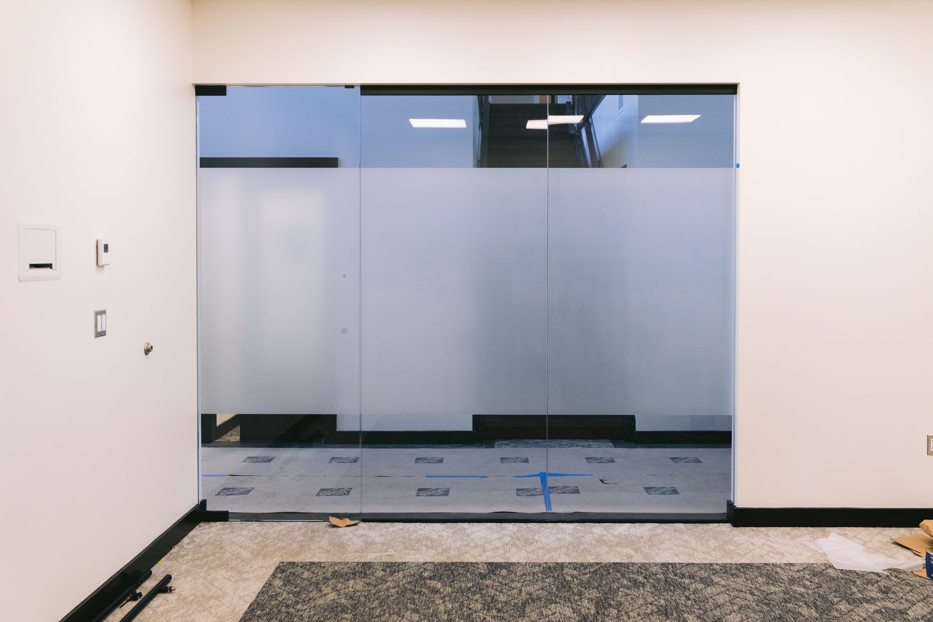 Modern glass double doors in a mostly empty room with protective floor covering