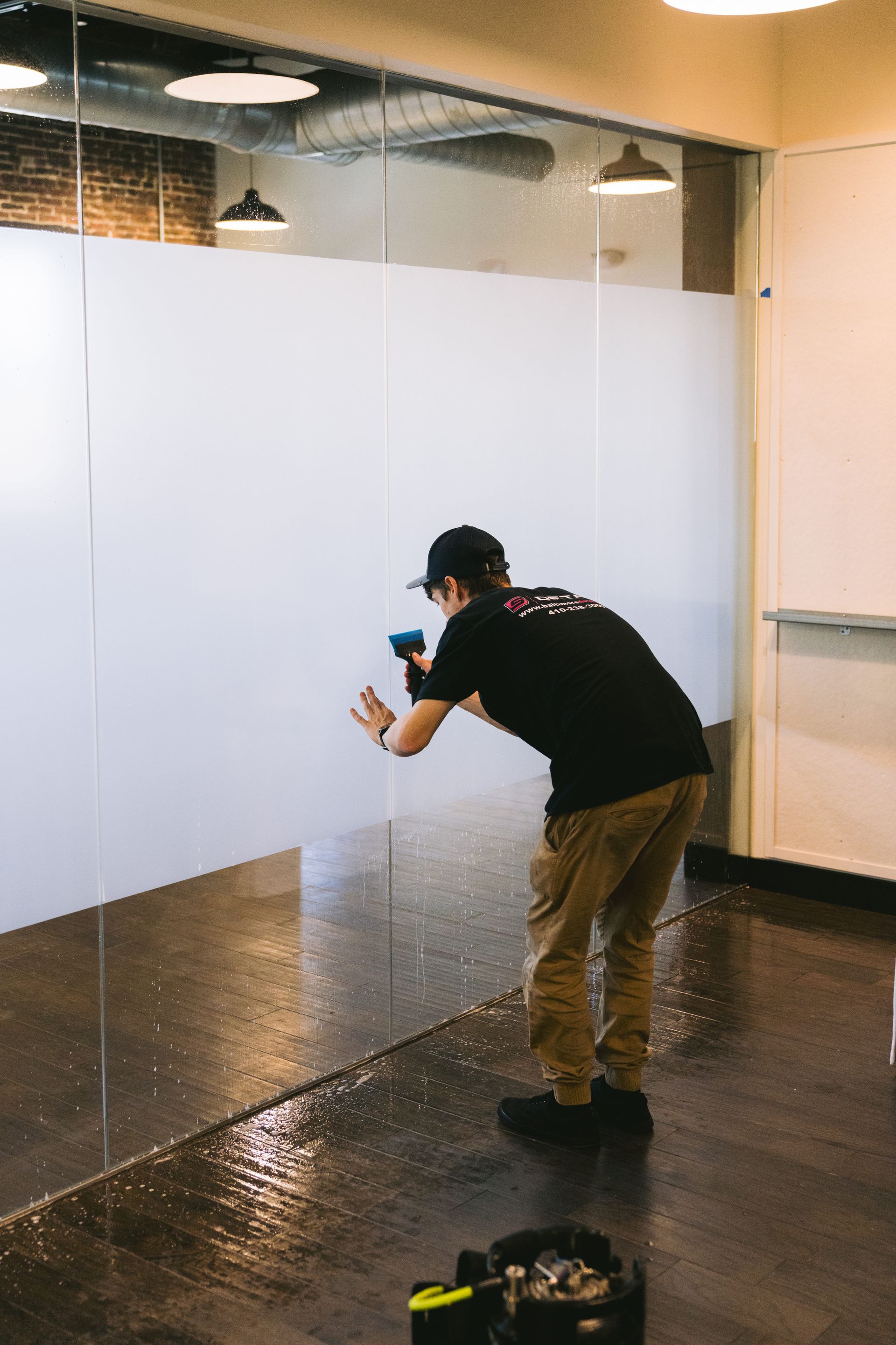 Person cleaning a glass wall in a modern office lobby with a spray bottle and cloth.