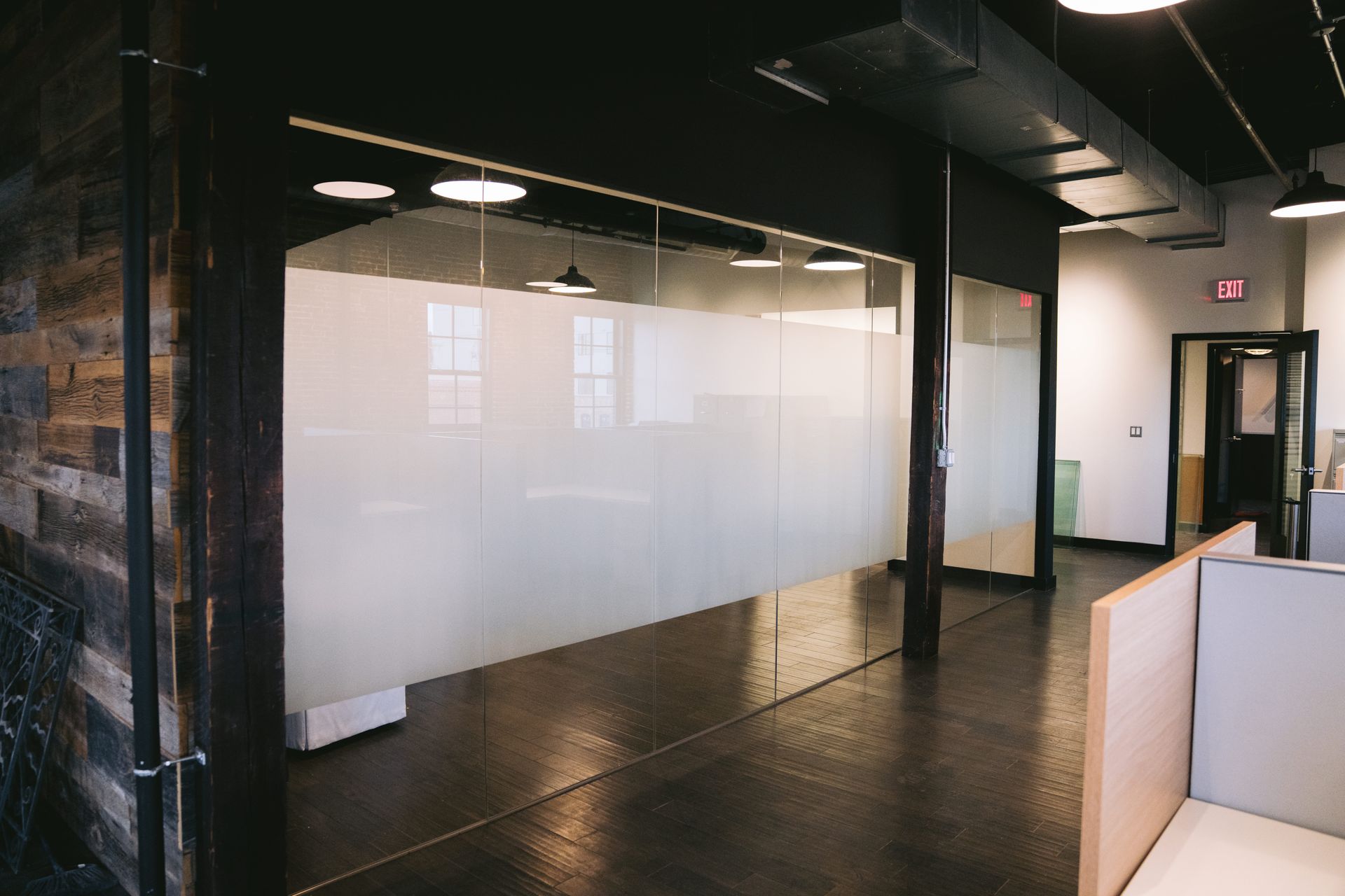 Modern office interior with glass walls, dark floors, and white partitions along a hallway