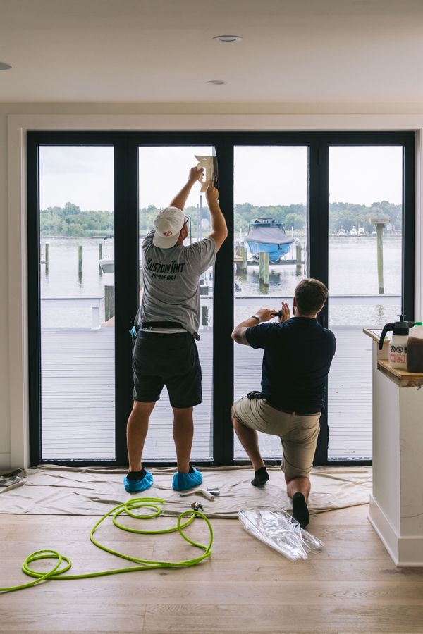 Two people installing a sliding glass door by the water, with tools and cables on the floor
