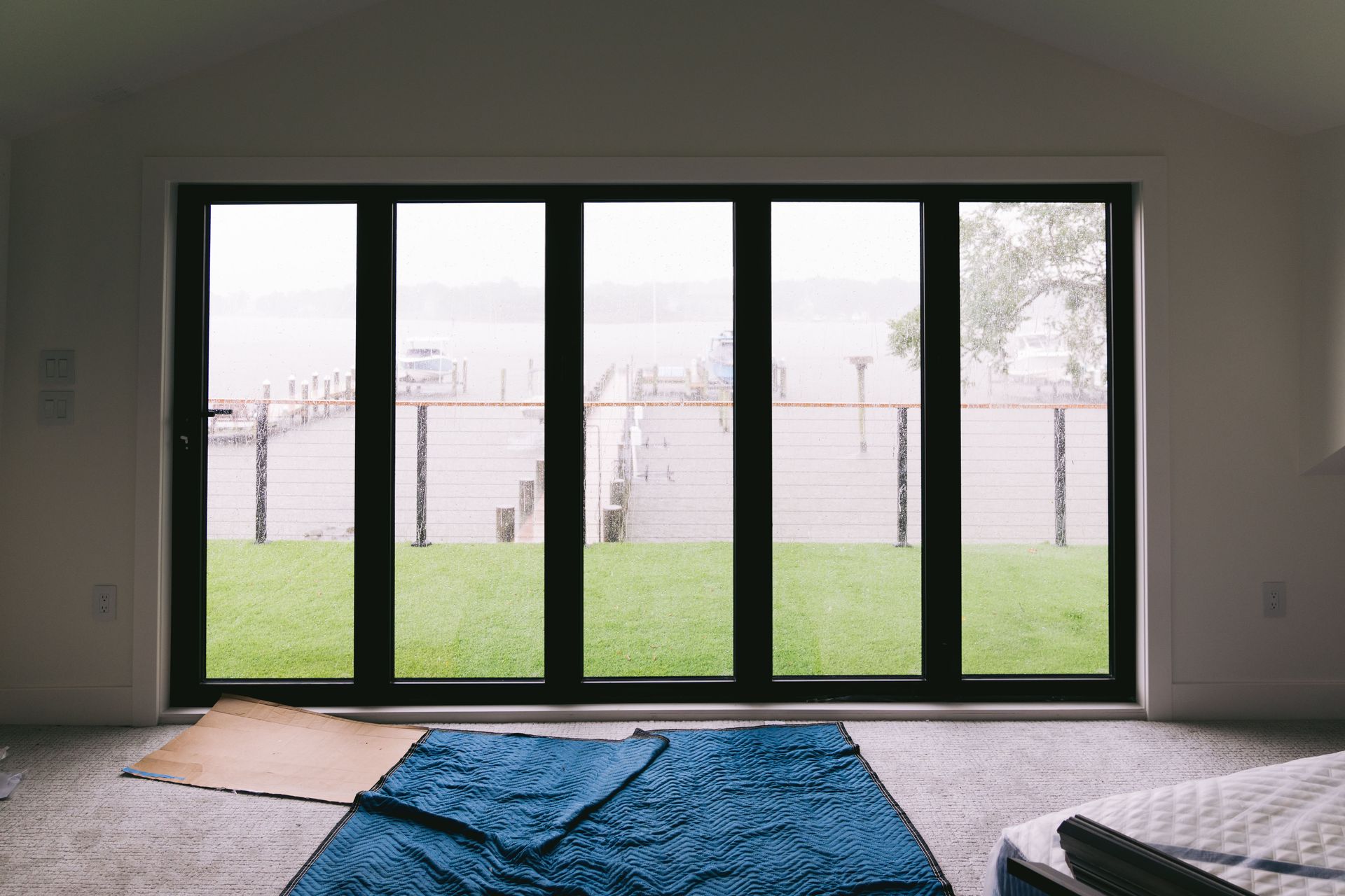 Empty room with large glass doors, green lawn outside, and rugs on the floor.