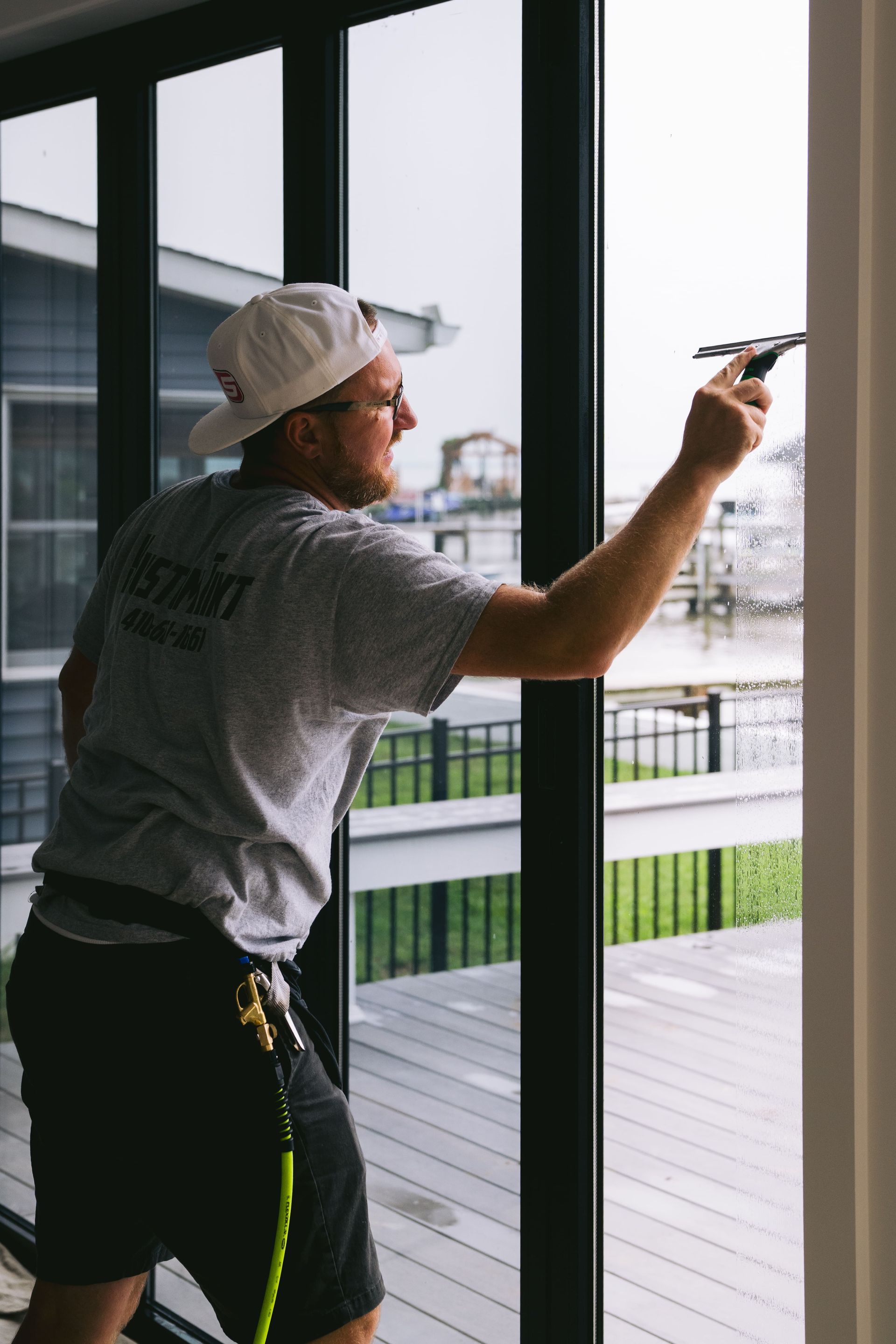 Person in a cap painting a window frame indoors with a small roller, with a city view outside