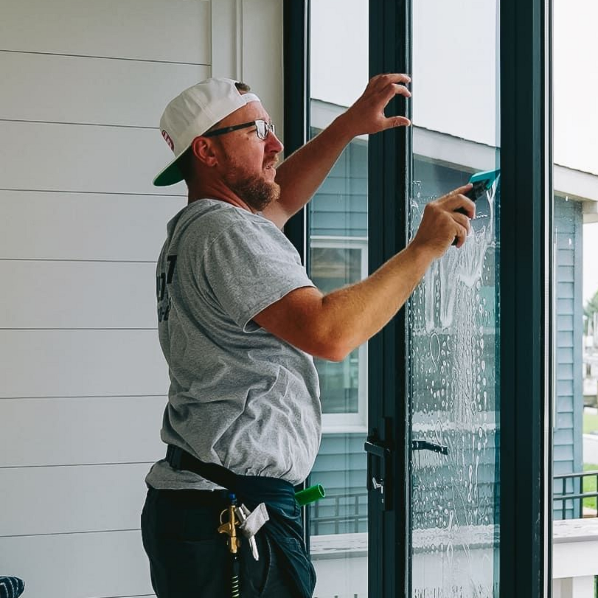 Worker cleaning a glass window with a spray bottle and squeegee on a balcony