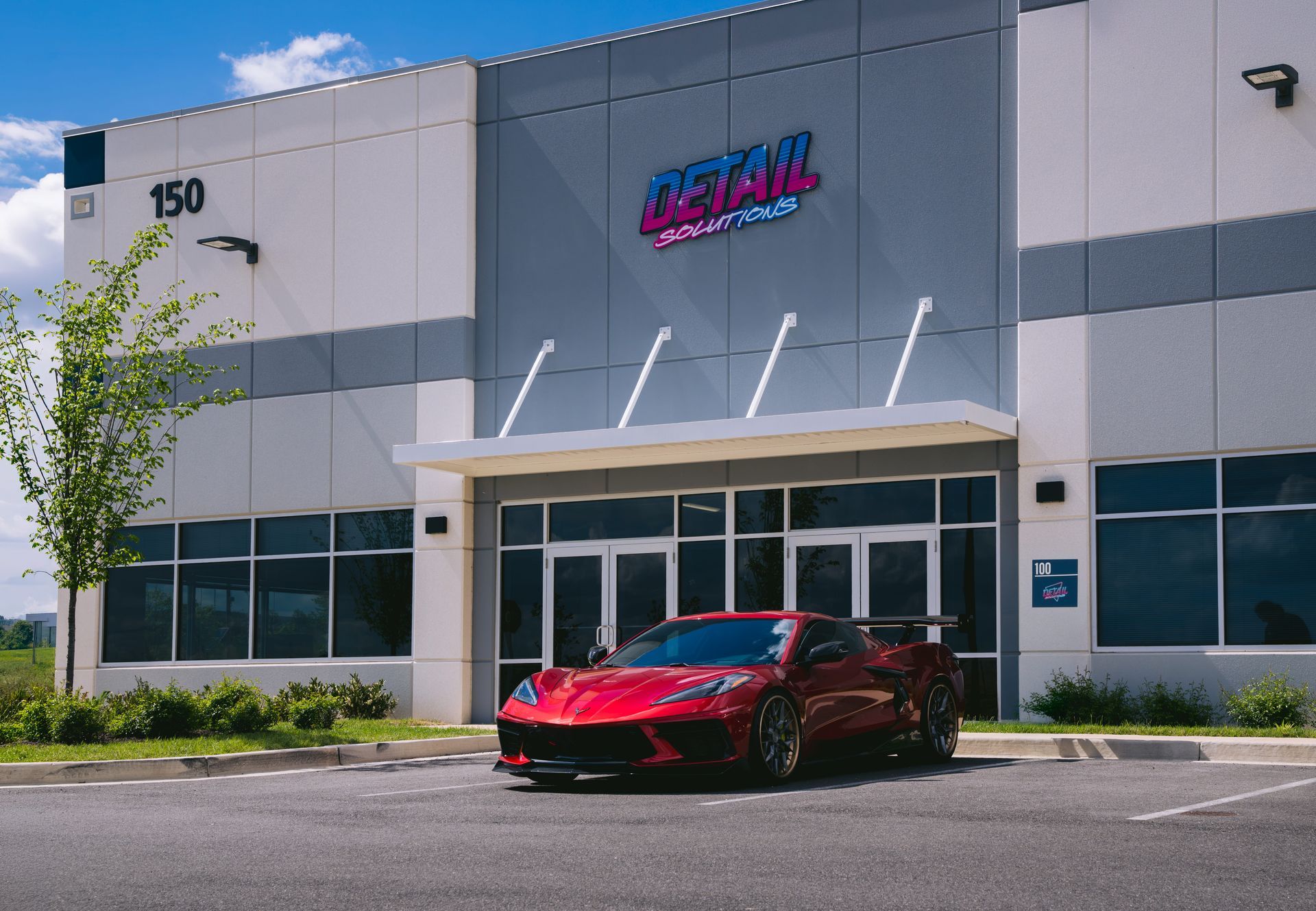 Red sports car parked outside a modern commercial building with a sign above the entrance