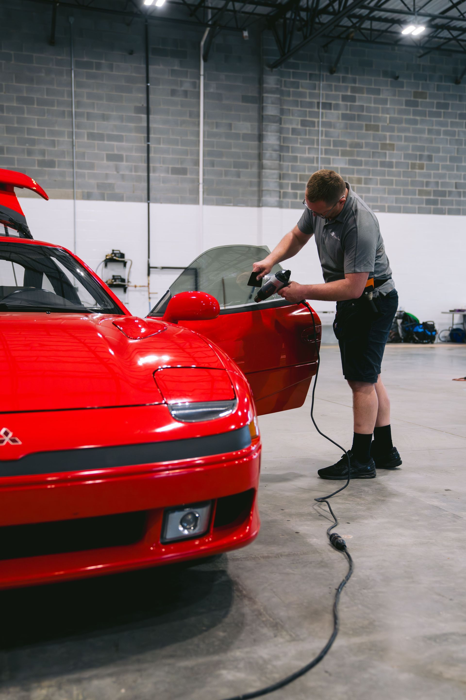 Man polishing the red door of a red sports car in a garage