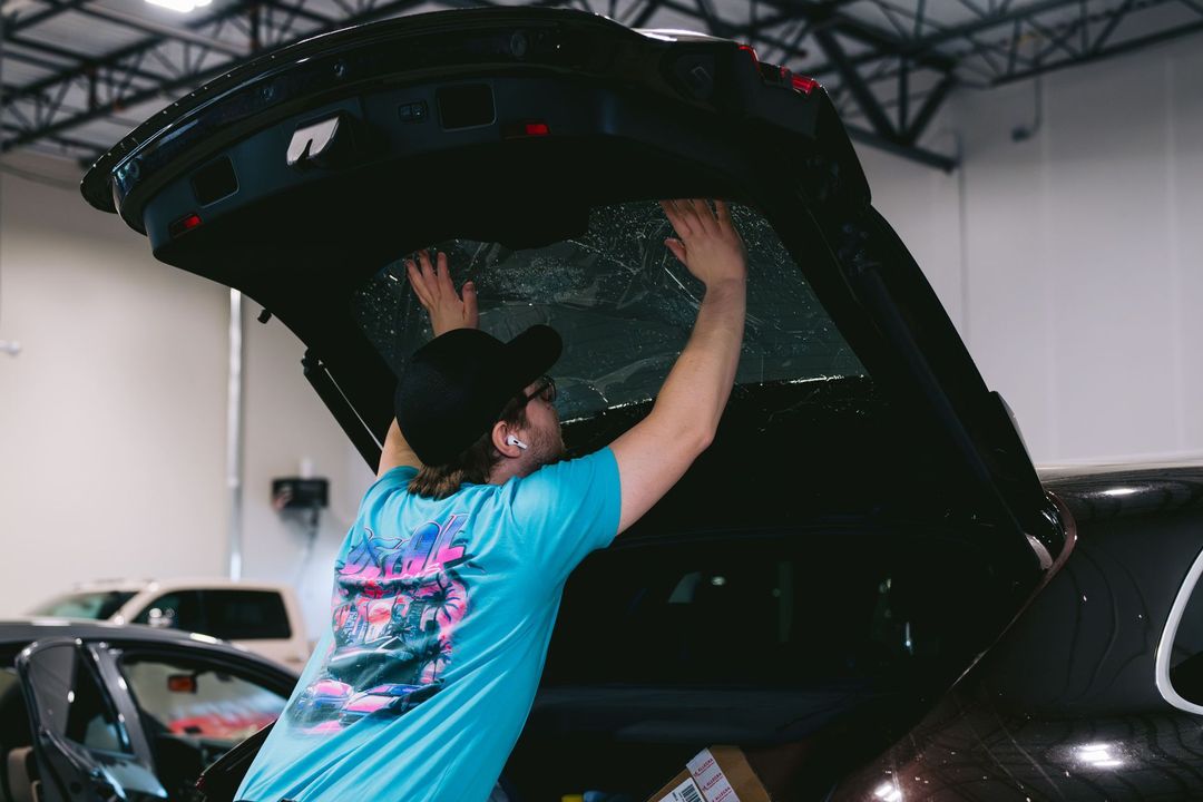 Person in a blue shirt lifts a car hatch in a garage, revealing equipment inside.