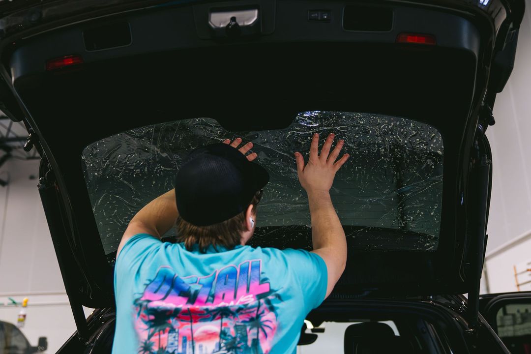 Person placing a shattered rear window into the open trunk of a car