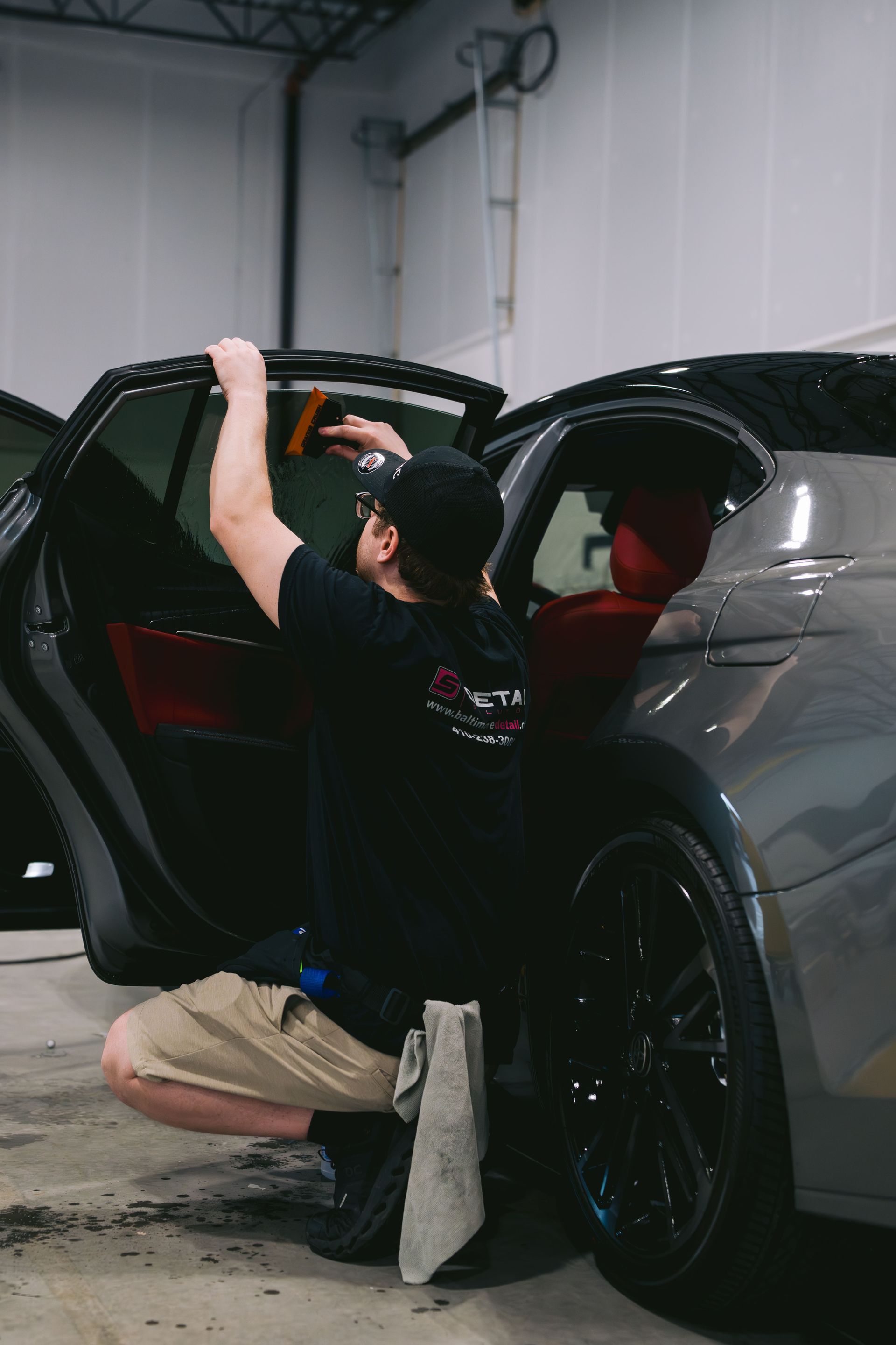 Person kneeling beside a gray SUV, reaching into the open rear door in a garage.