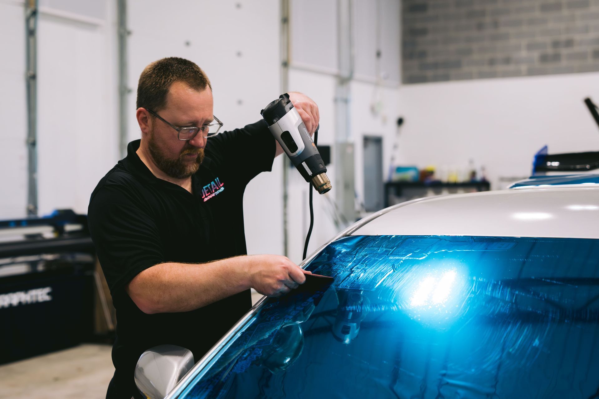 Technician using a polisher on a blue car windshield in a garage