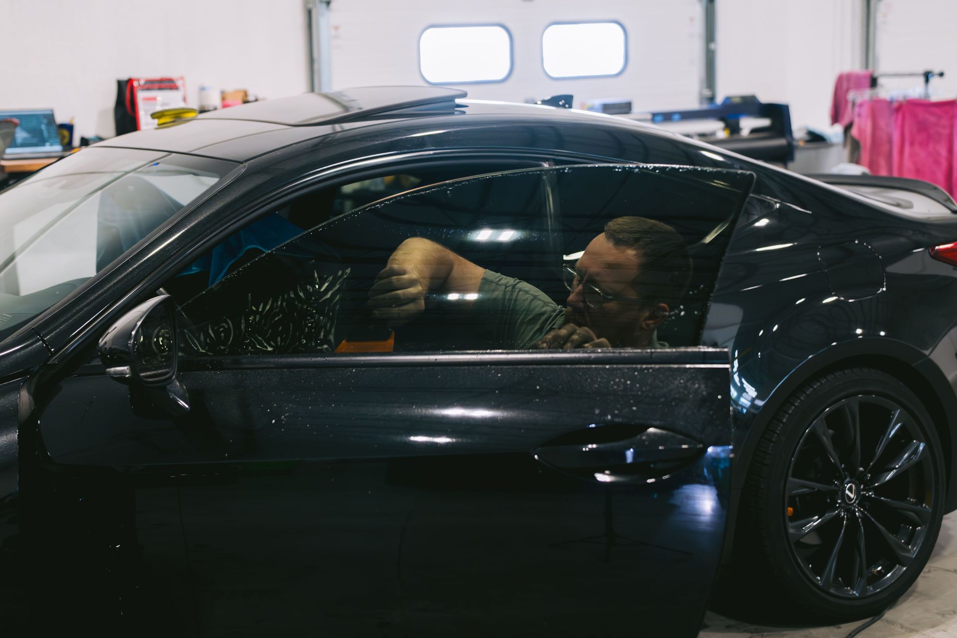 Black sports car in a garage with two people visible inside, viewed from the side