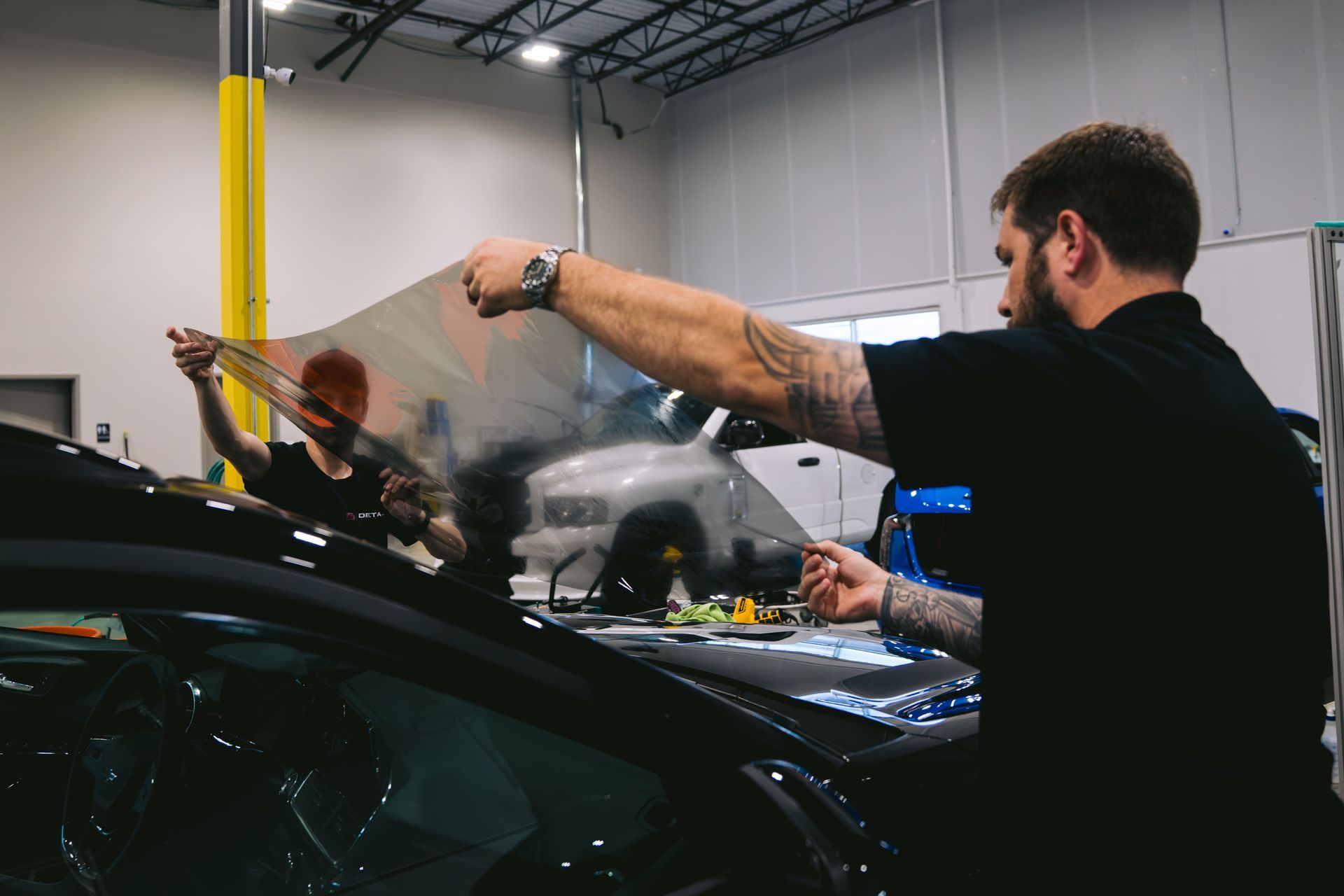 Auto detailer polishing a black car with a buffer in a workshop