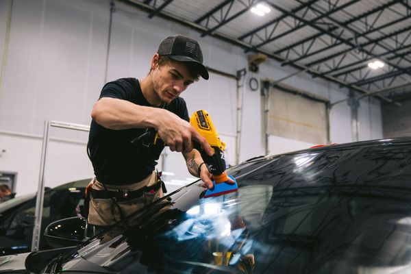 Technician using a yellow tool to remove debris from a car windshield in a garage