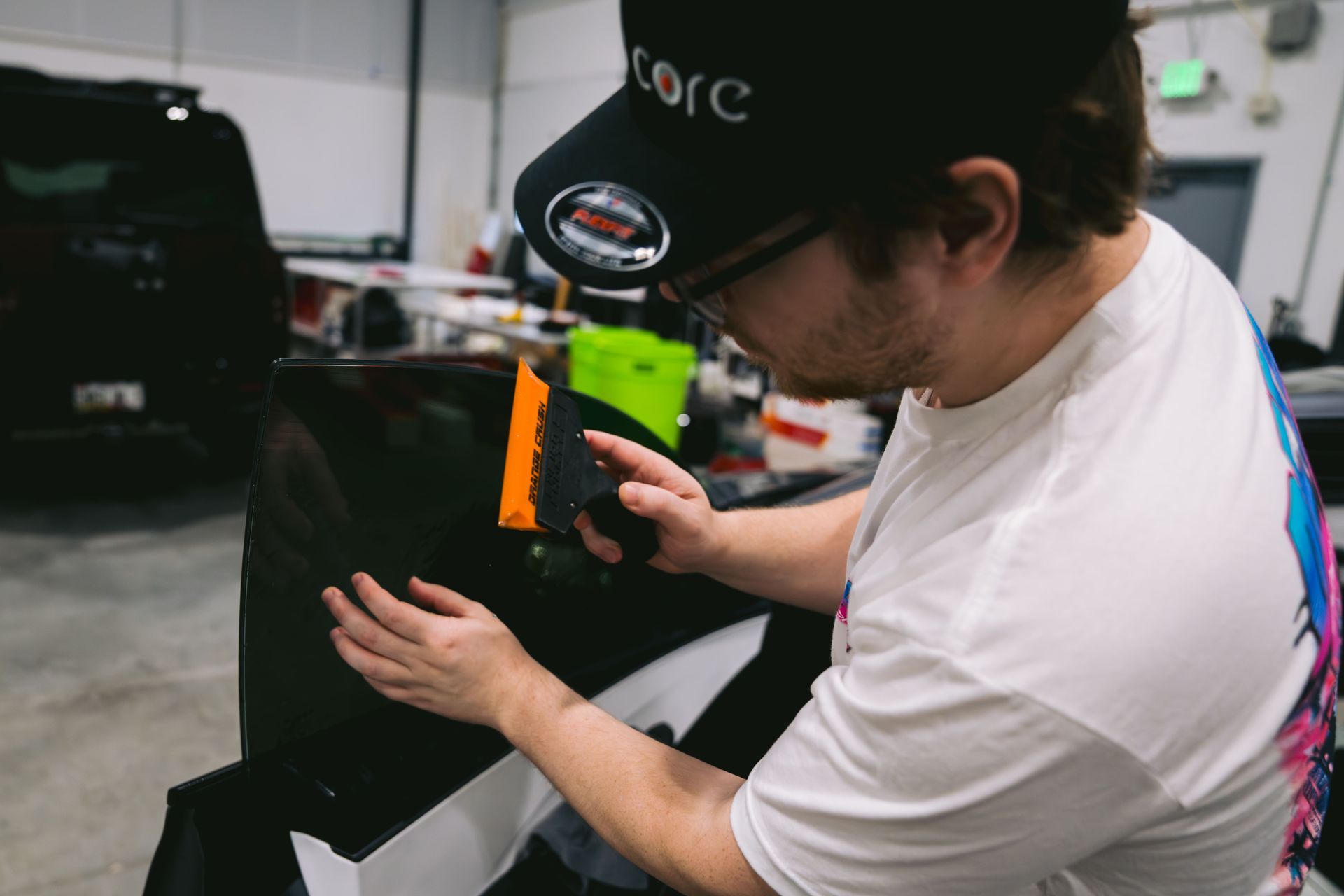 Person in a black cap adjusting equipment in a workshop, with a black bag and tools nearby.