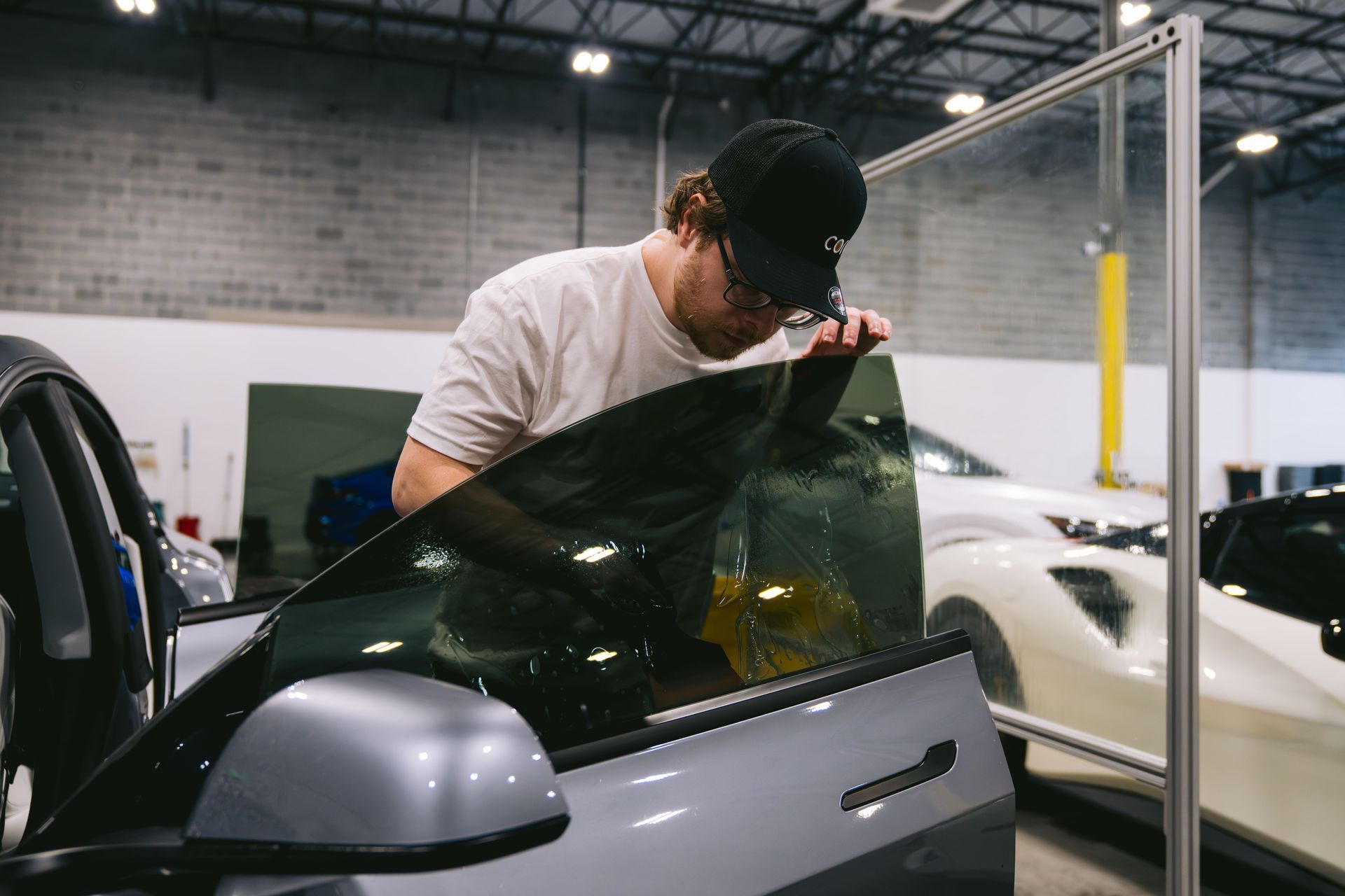 Technician installing tinted film on a car window in an auto shop