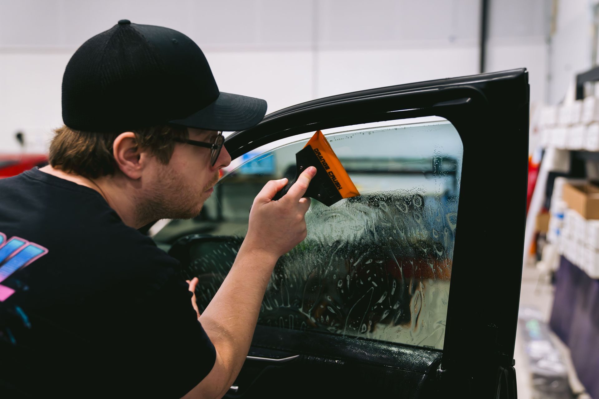 Person using a squeegee to clean a car window indoors