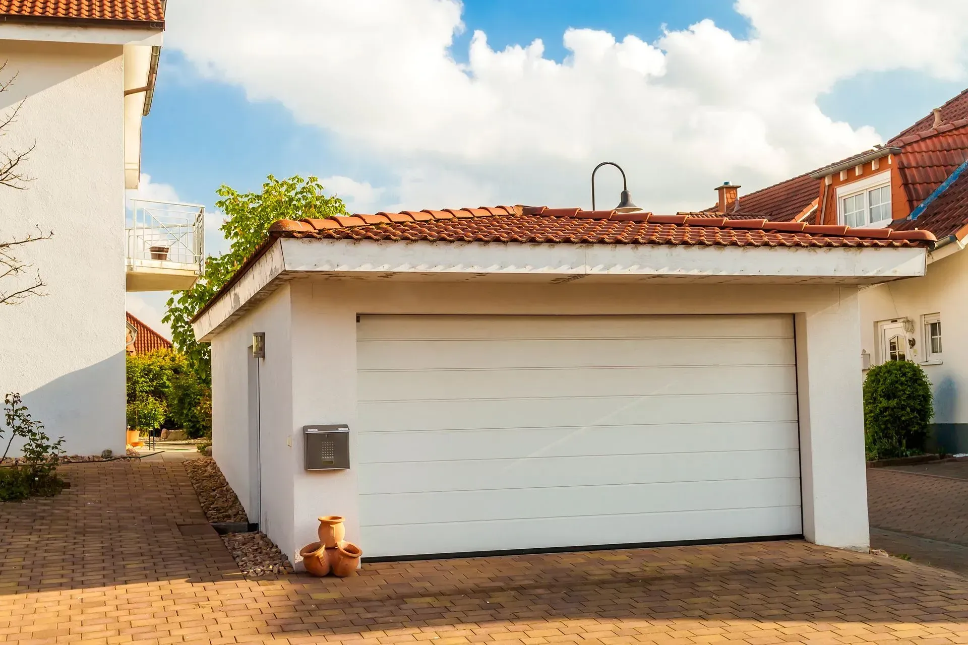 White garage with closed door, brown tile roof, next to a white house, on a sunny day. White garage with closed door, brown tile roof, next to a white house, on a sunny day.