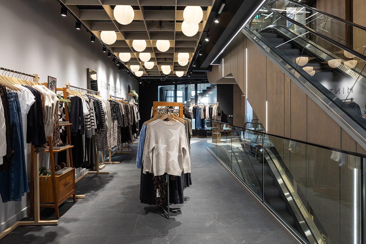 Clothing store interior with clothing racks, a timber effect clad staircase, and decorative lighting.