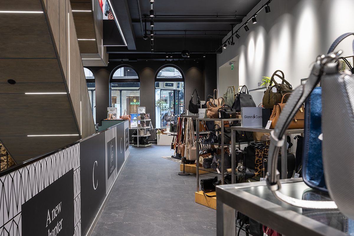 No 13 Creaseys interior shop view with bags and scarves on display racks, dark ceiling, and a concrete staircase on the left.