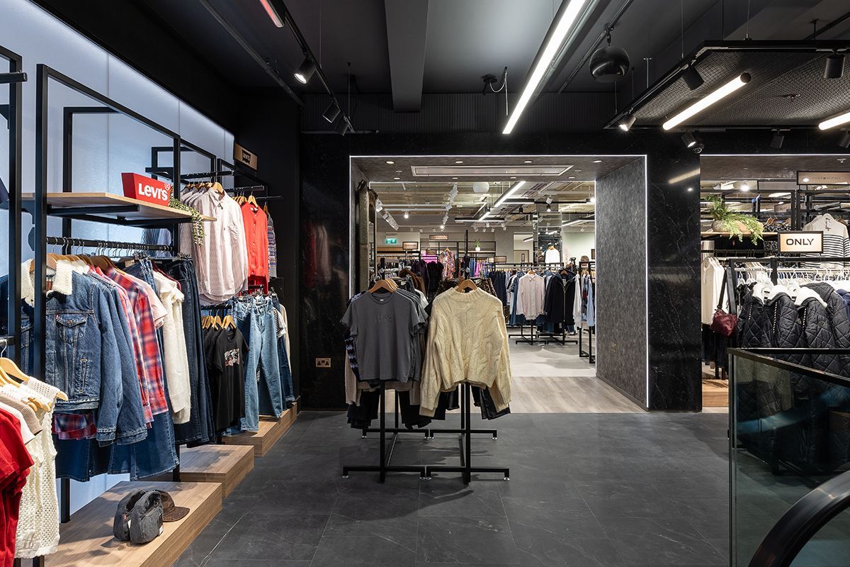 Clothing store interior with clothing racks, dark walls, and bright overhead lights.