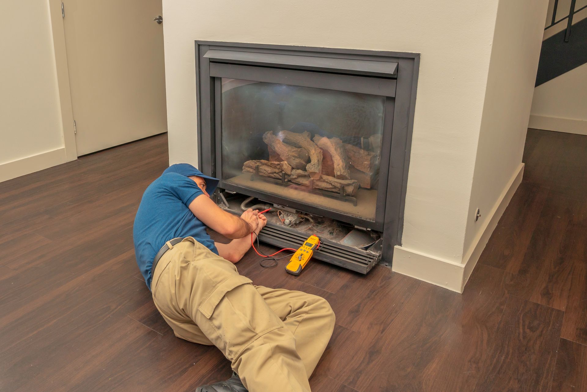 Person lying on a hardwood floor in front of a fireplace, working with a yellow tool.
