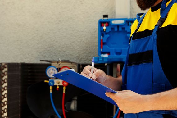 Worker in blue and yellow uniform writing on a clipboard in a workshop, with machinery in the background