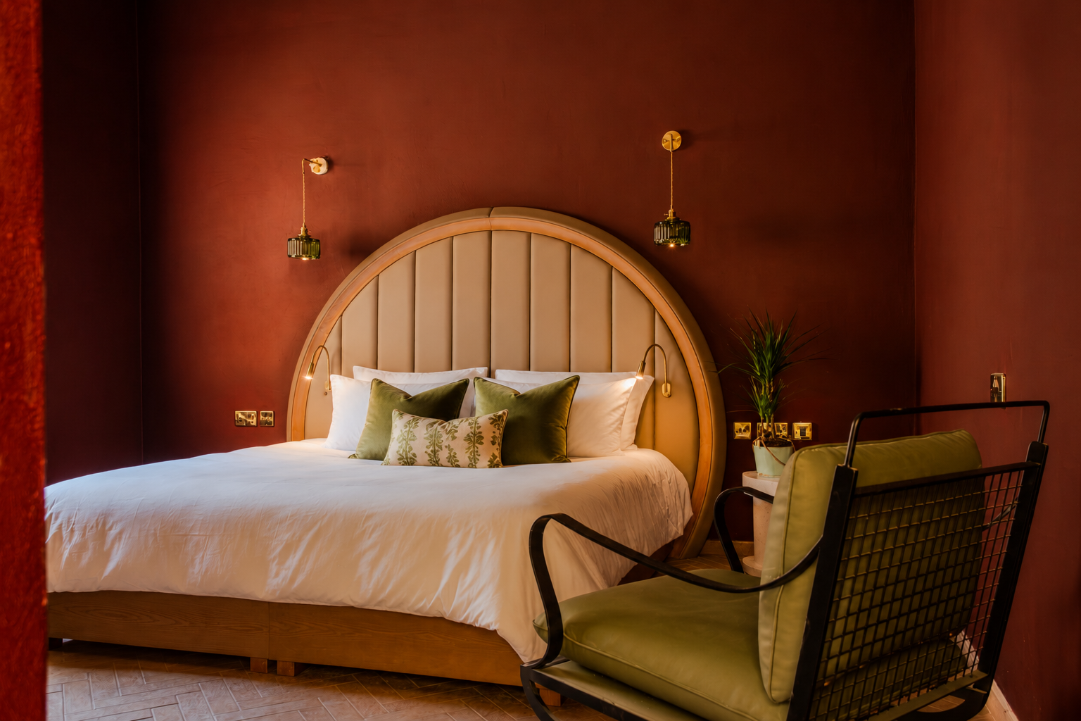 Elegant bedroom with a round wooden headboard, white bedding, red walls, and a green armchair