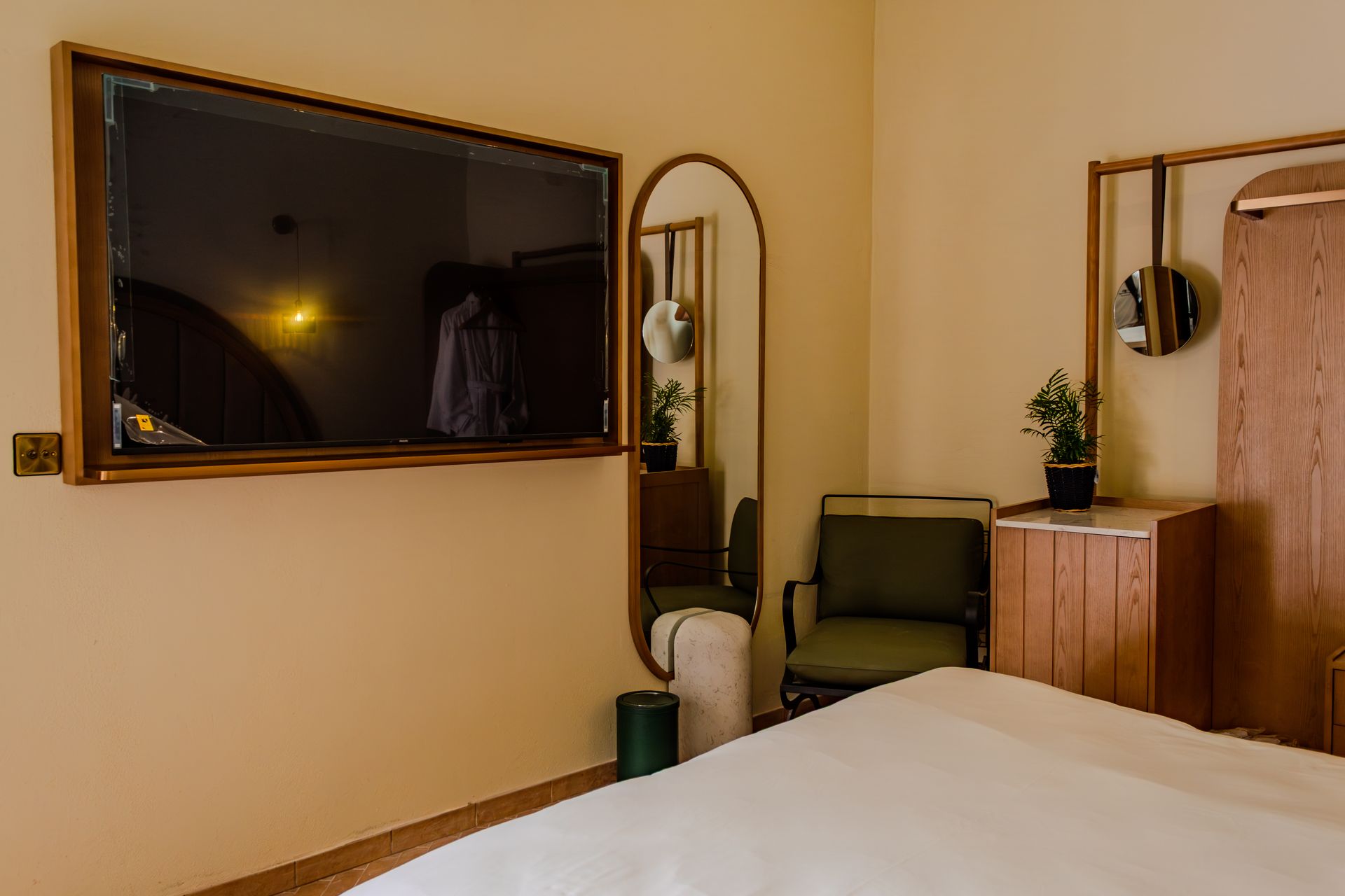 Bedroom with wall-mounted TV, mirror, chair, and dresser beside a bed