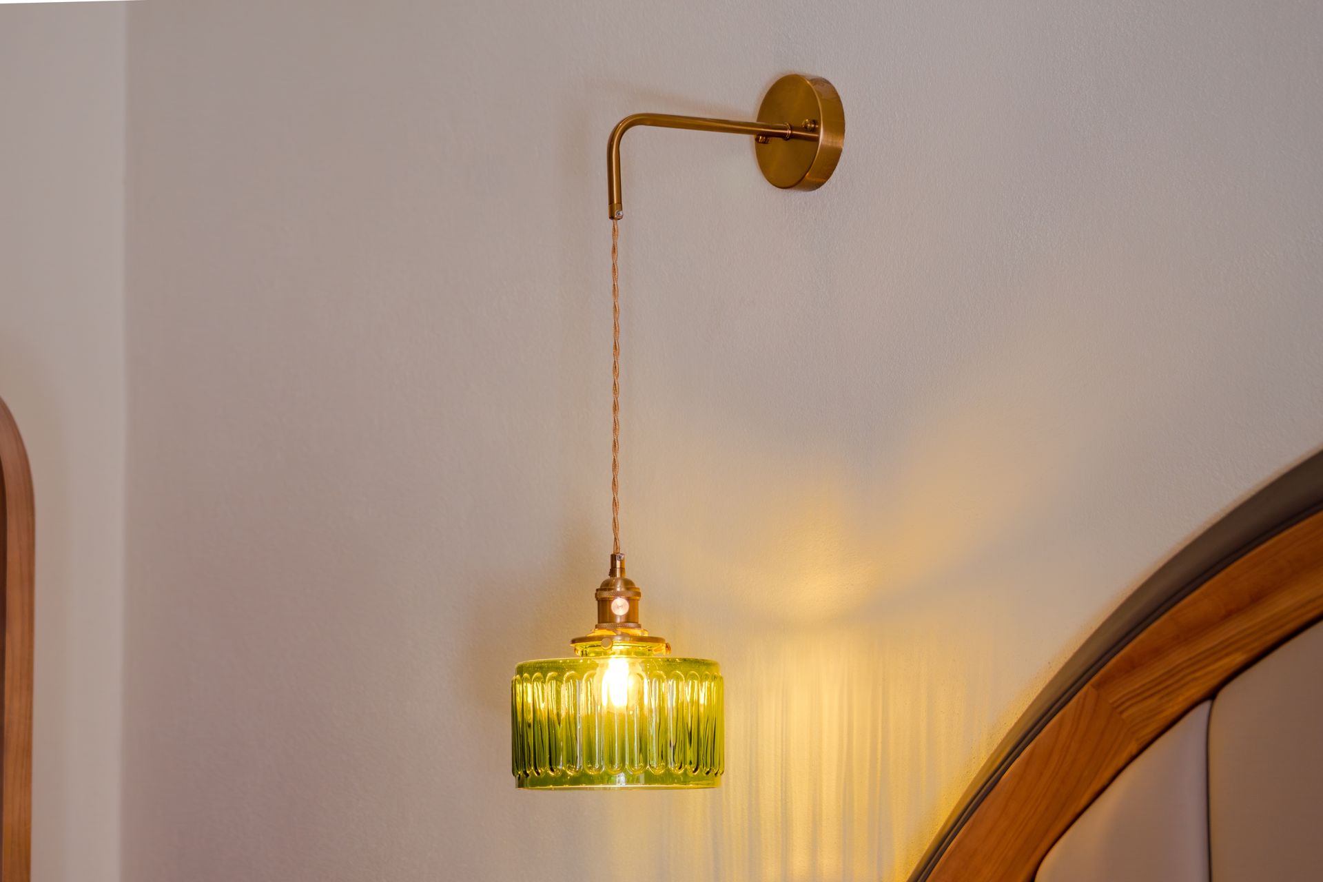 Green glass pendant lamp hanging from a brass wall mount in a softly lit room.