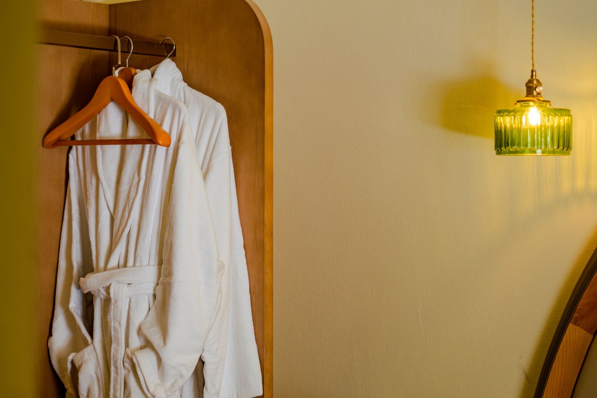 White bathrobes on wooden hangers in a closet beside a glowing green pendant lamp