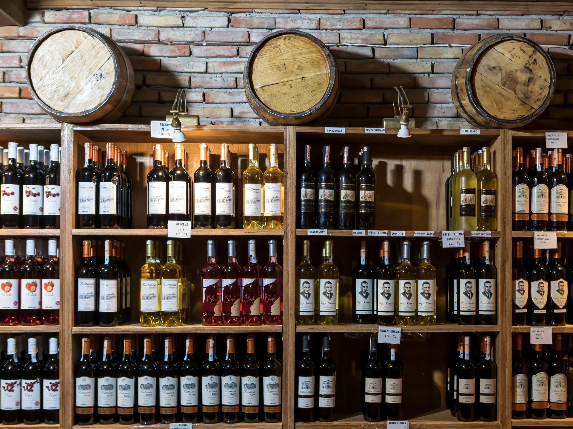 Wine bottles displayed on wooden shelves against a brick wall with three barrel-style clocks above.