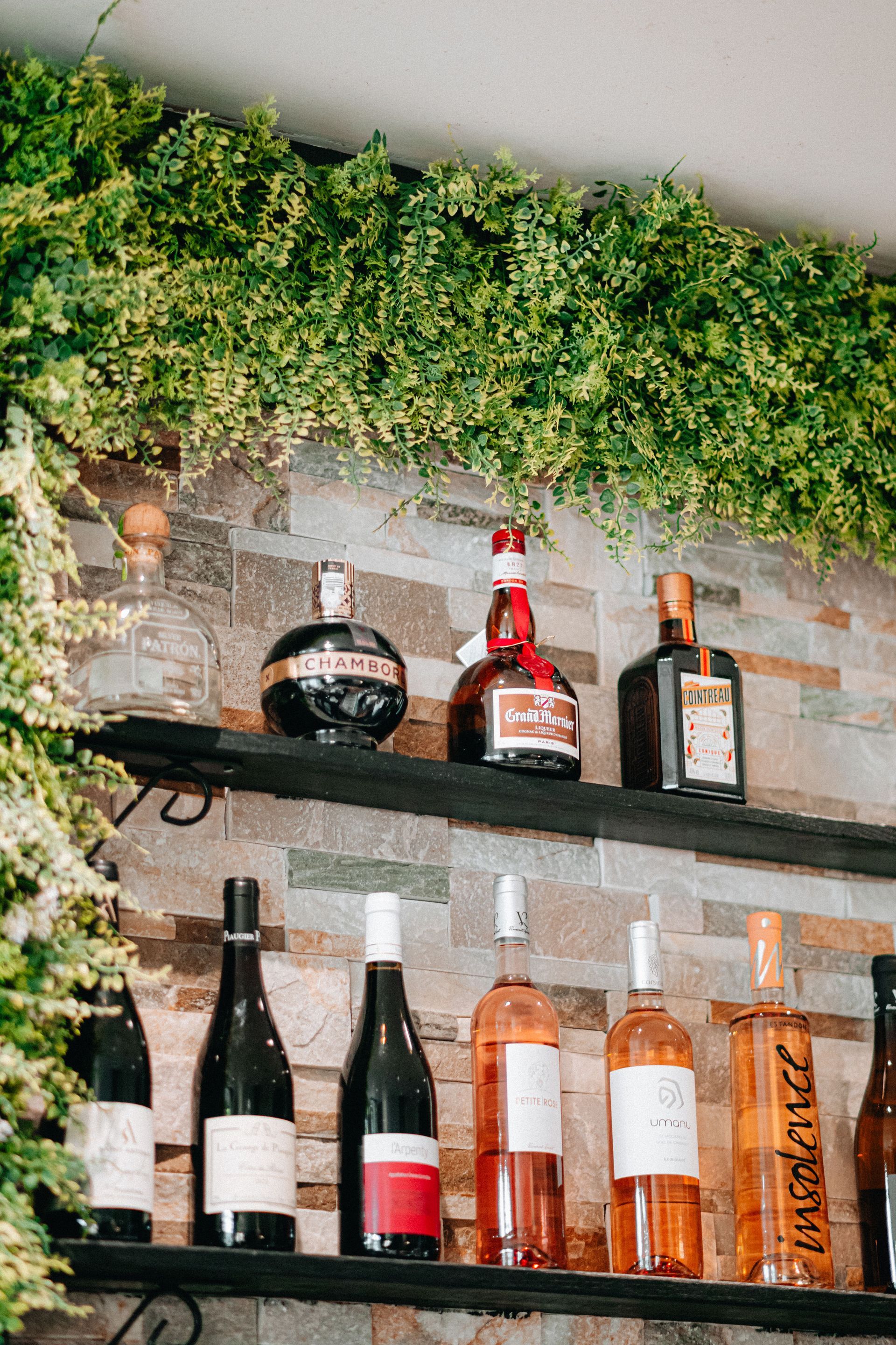 Shelves of liquor bottles against a brick wall with hanging green foliage above