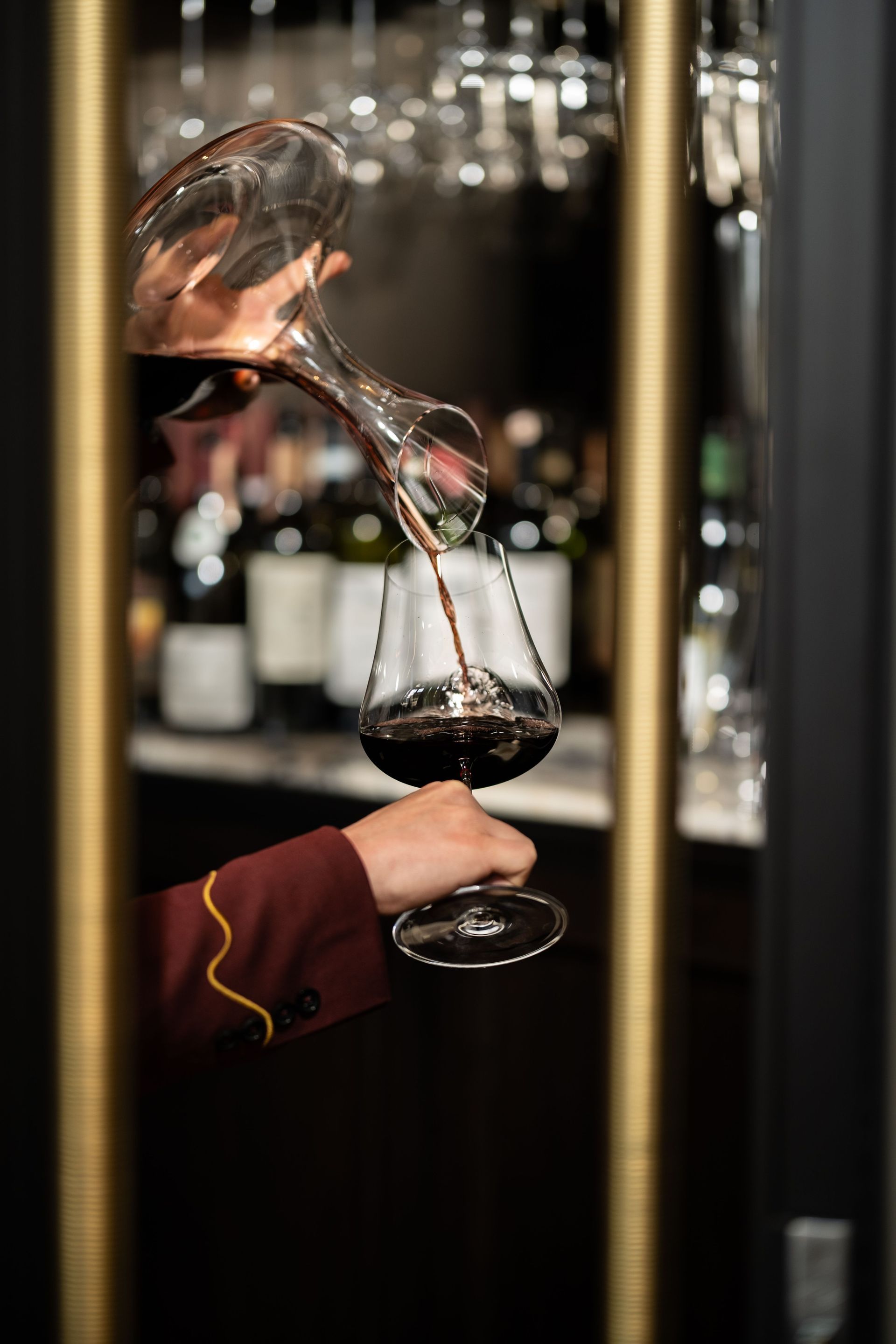 A hand pours red wine into a glass in a dimly lit wine cellar.
