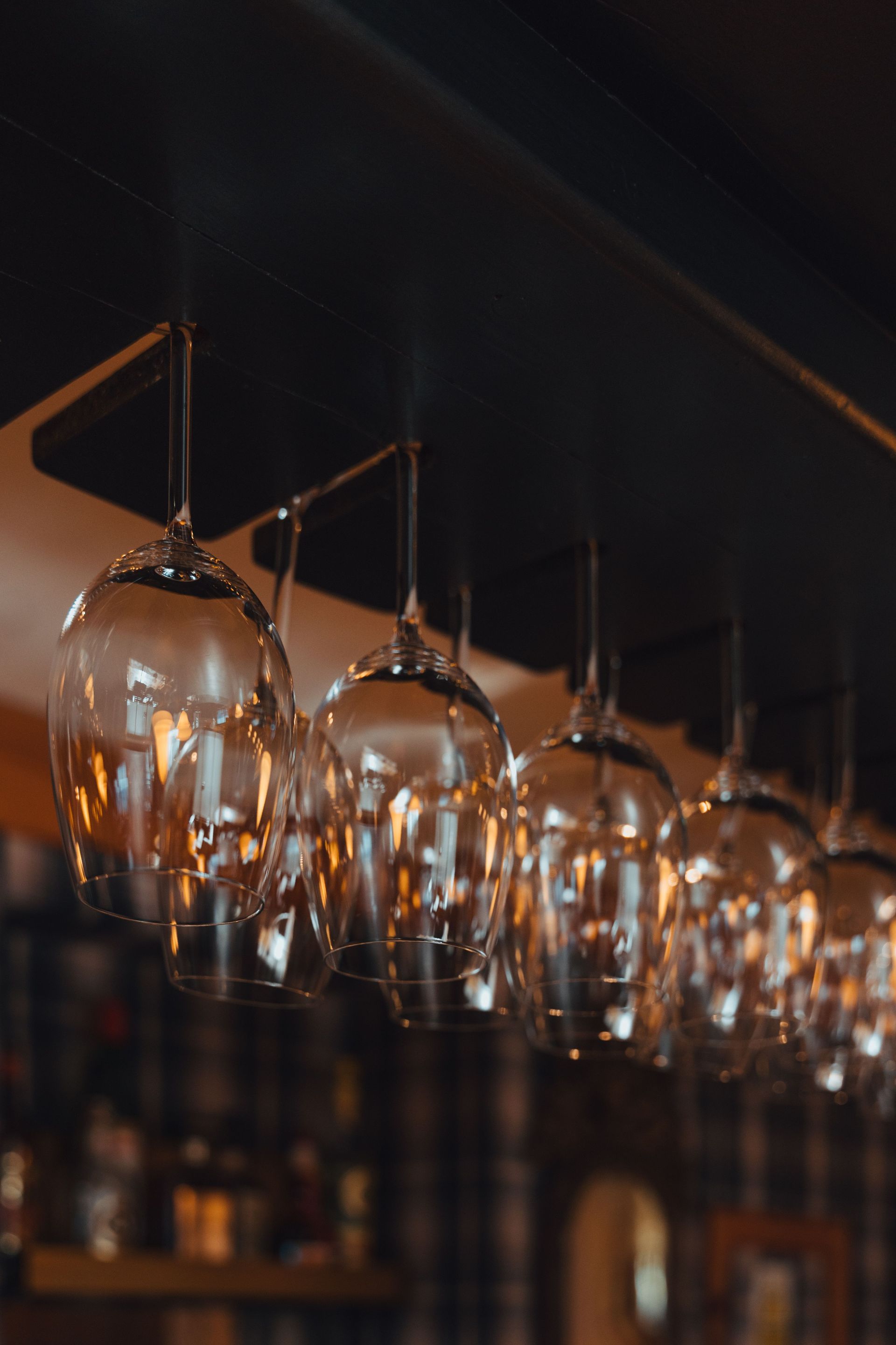 Row of upside-down wine glasses hanging in a dimly lit bar, with warm reflections on the glass.