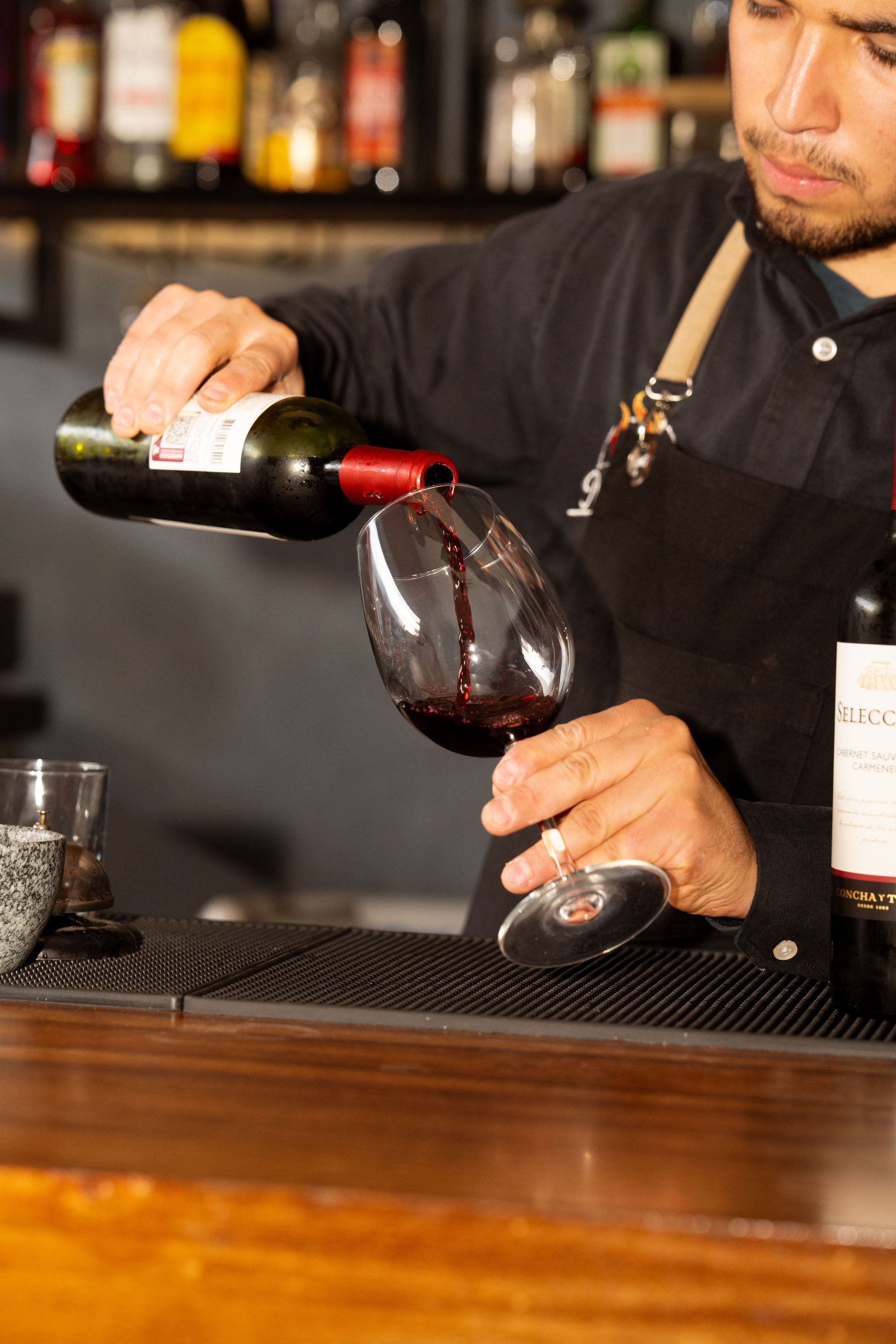 Bartender pouring red wine into a glass at a bar counter