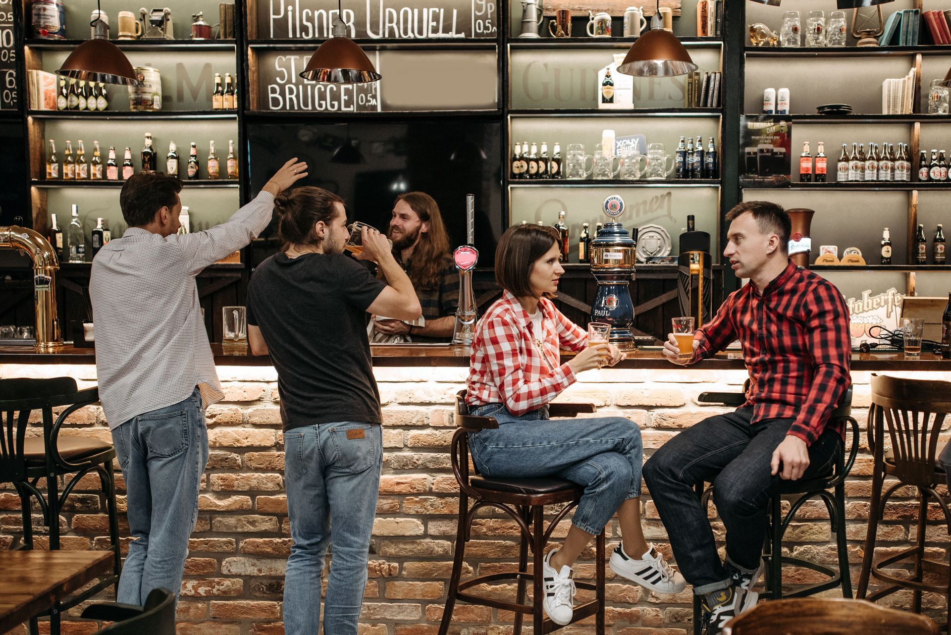 People talking in a rustic bar, with bottles on shelves and two couples seated at the counter.