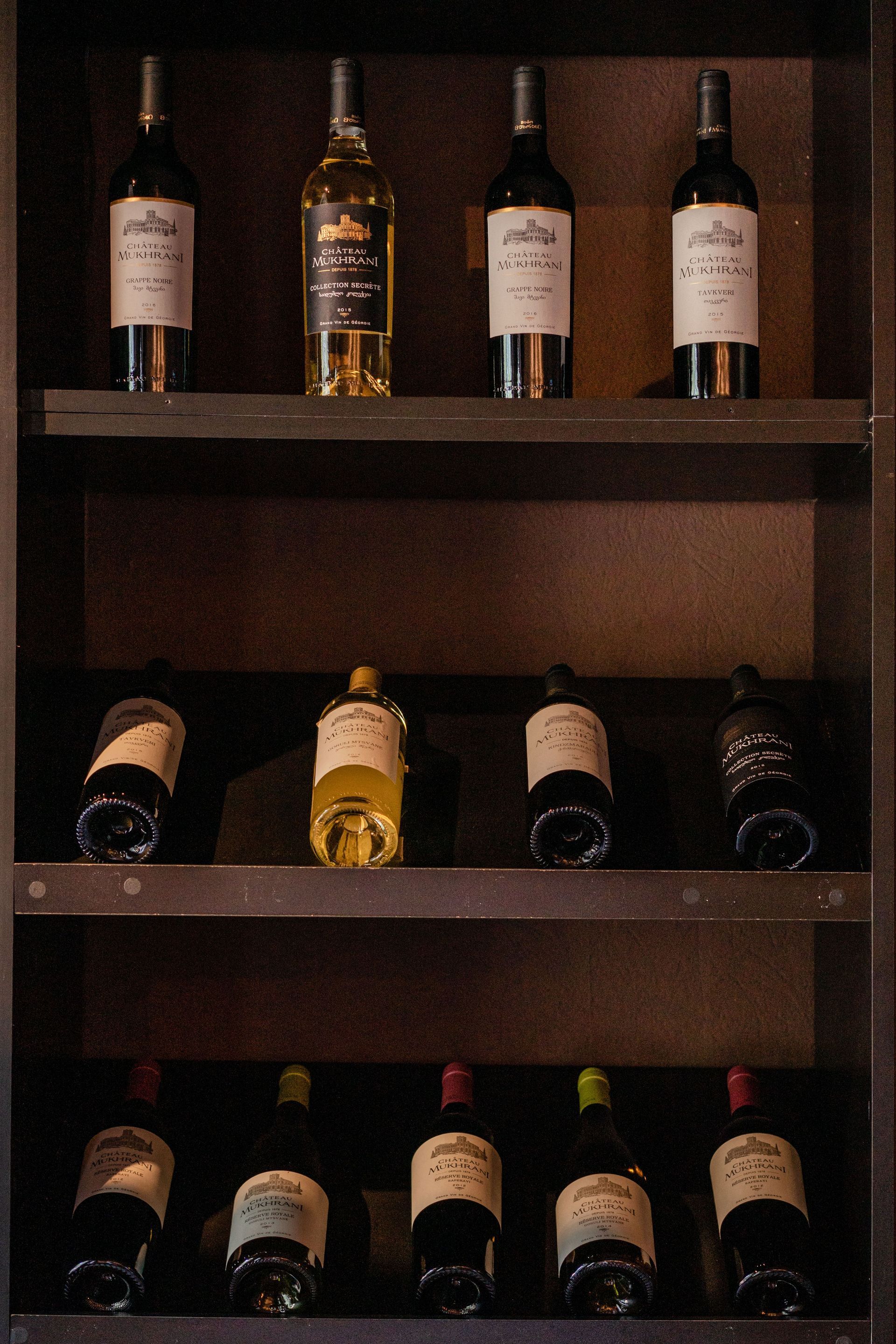 Wine bottles arranged on dark wooden shelves in a dimly lit display