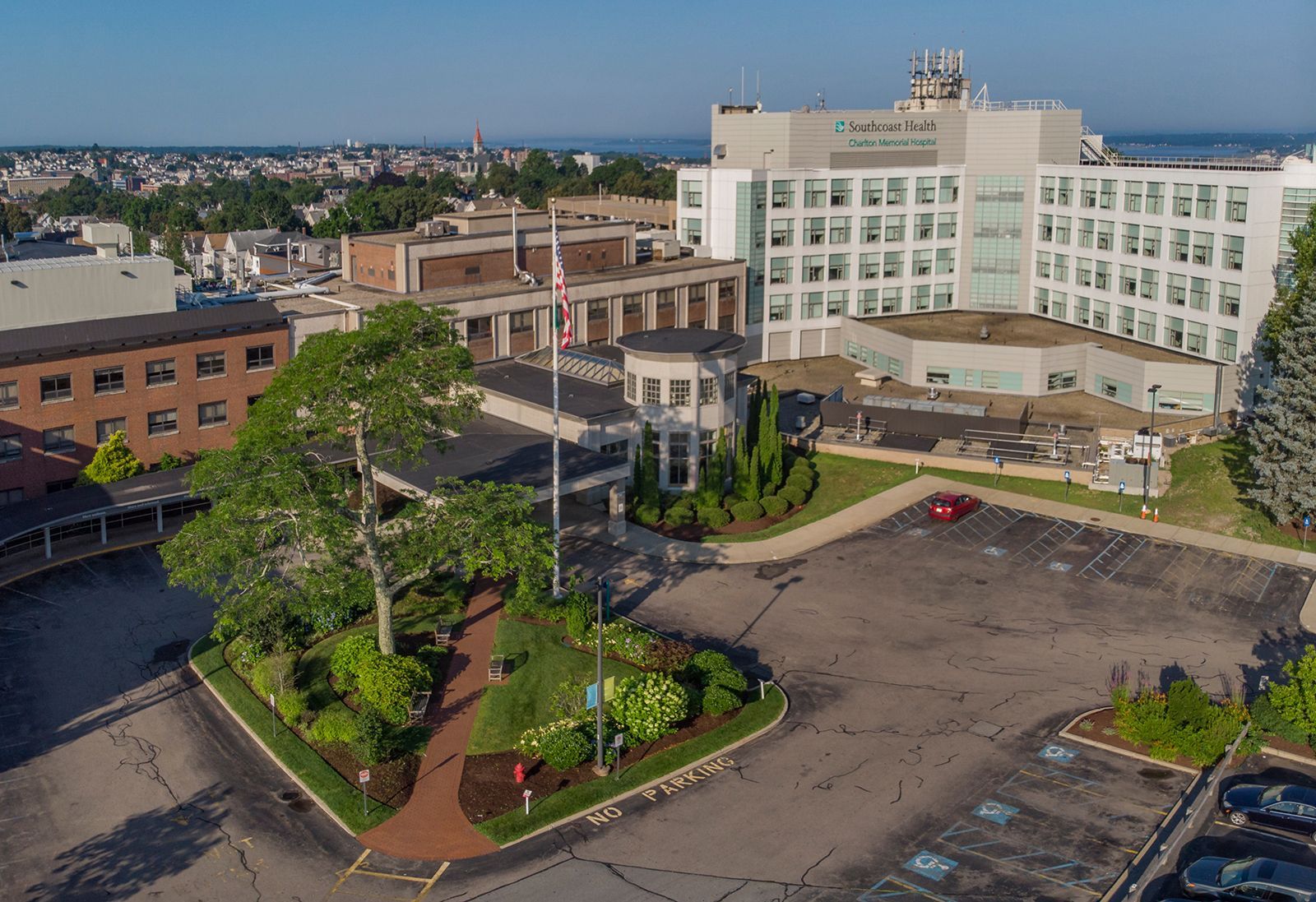 Aerial view of a hospital campus with white buildings, trees, and mostly empty parking lots.