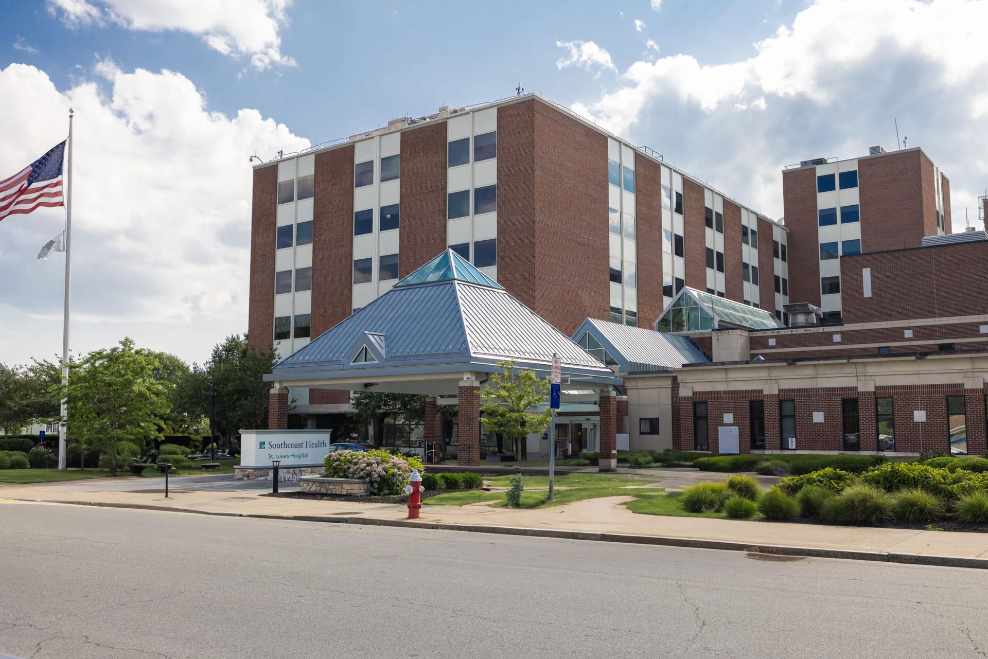 Hospital building entrance with blue-roofed canopy and an American flag outside