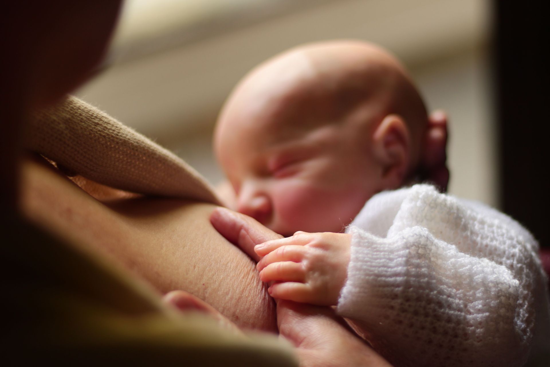Newborn baby breastfeeding, resting against a parent in a soft-lit close-up
