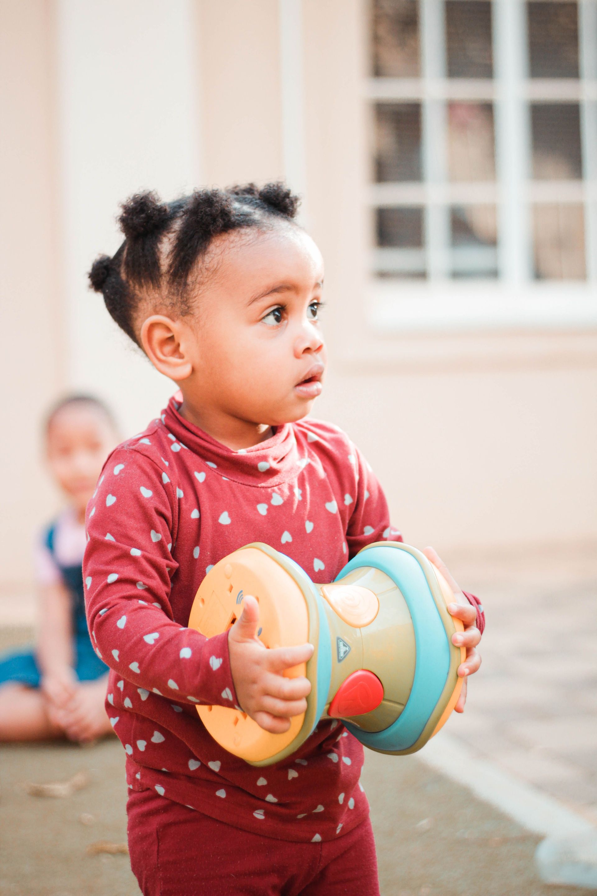 Toddler holding a colorful toy in a sunlit outdoor patio.