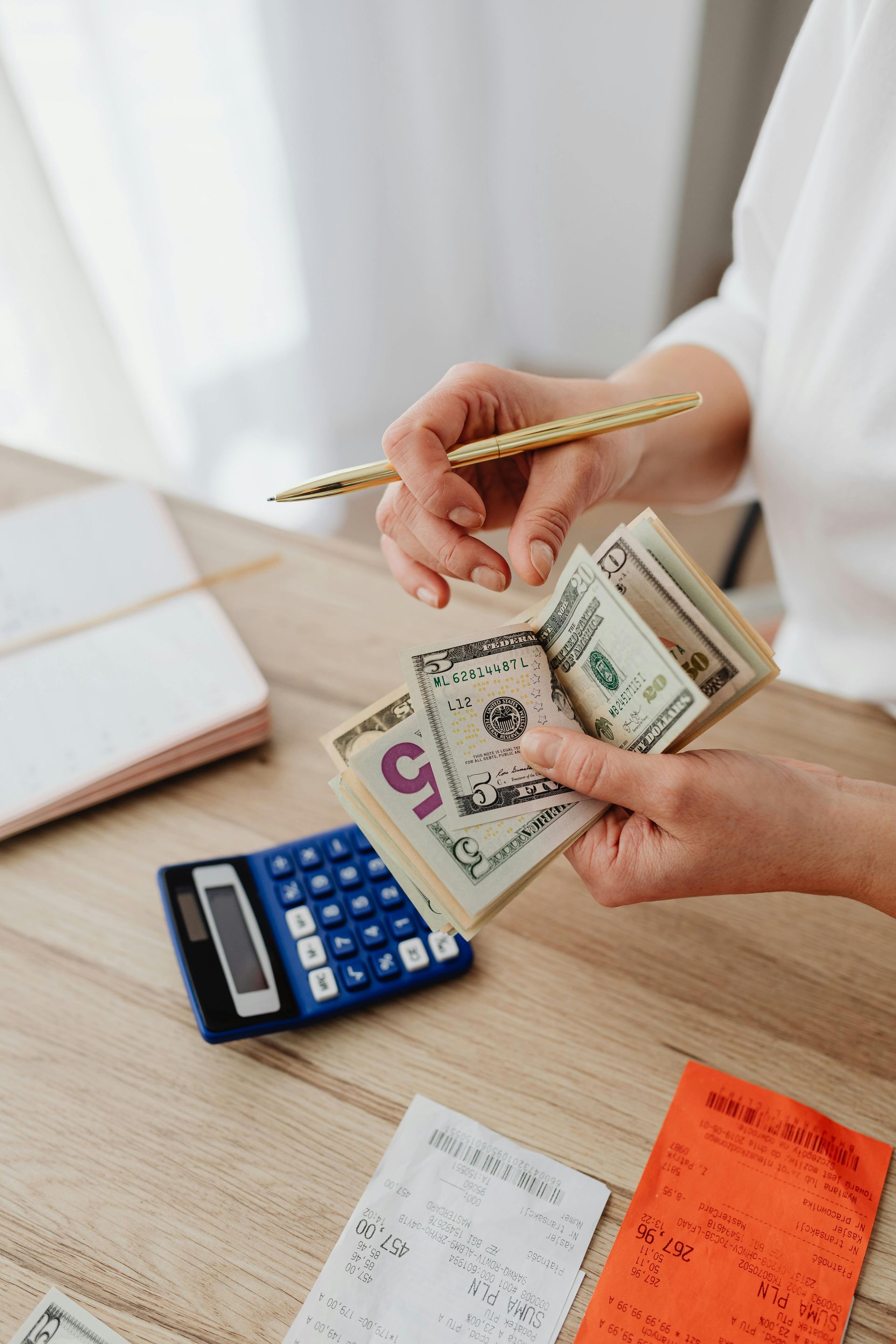 Hands counting cash beside a calculator and receipts on a desk