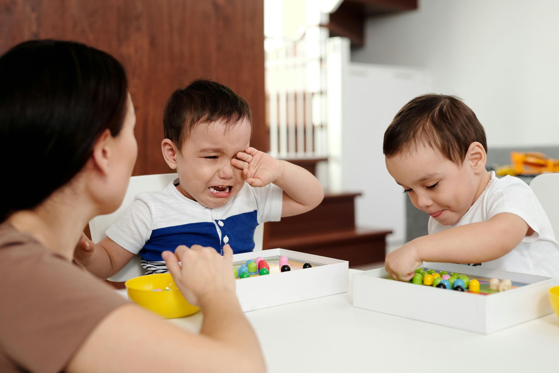 Adult and two children play with colorful blocks at a table, one child laughing in a bright room