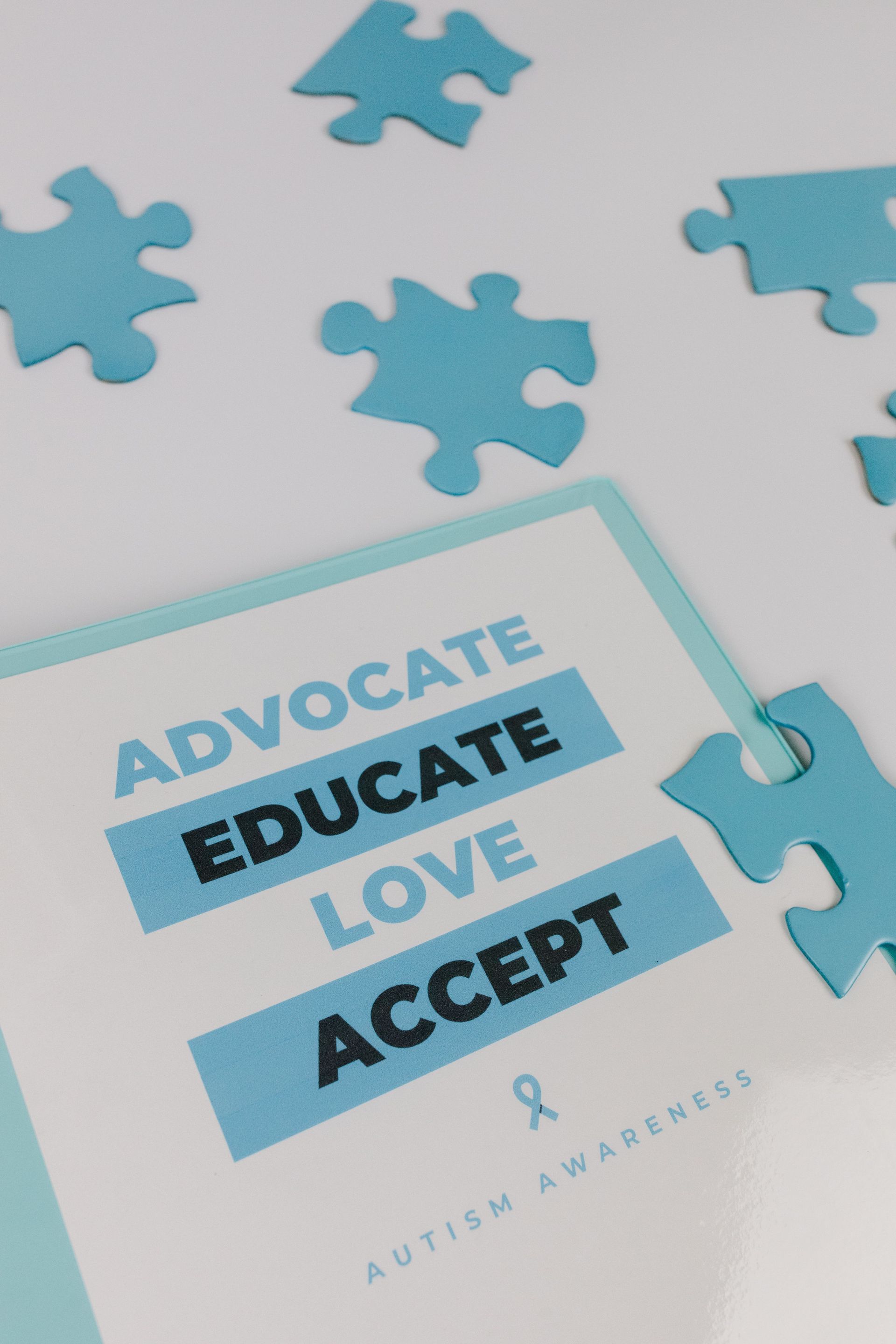Puzzle pieces with a card reading “ADVOCATE, EDUCATE, LOVE, ACCEPT” on a light background.