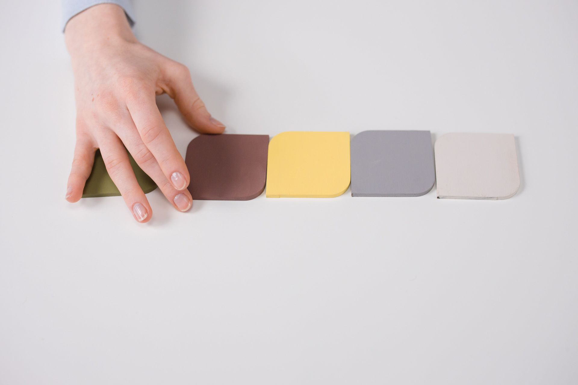 Hand placing a brown tile beside a row of brown, yellow, gray, and white square tiles on a white surface