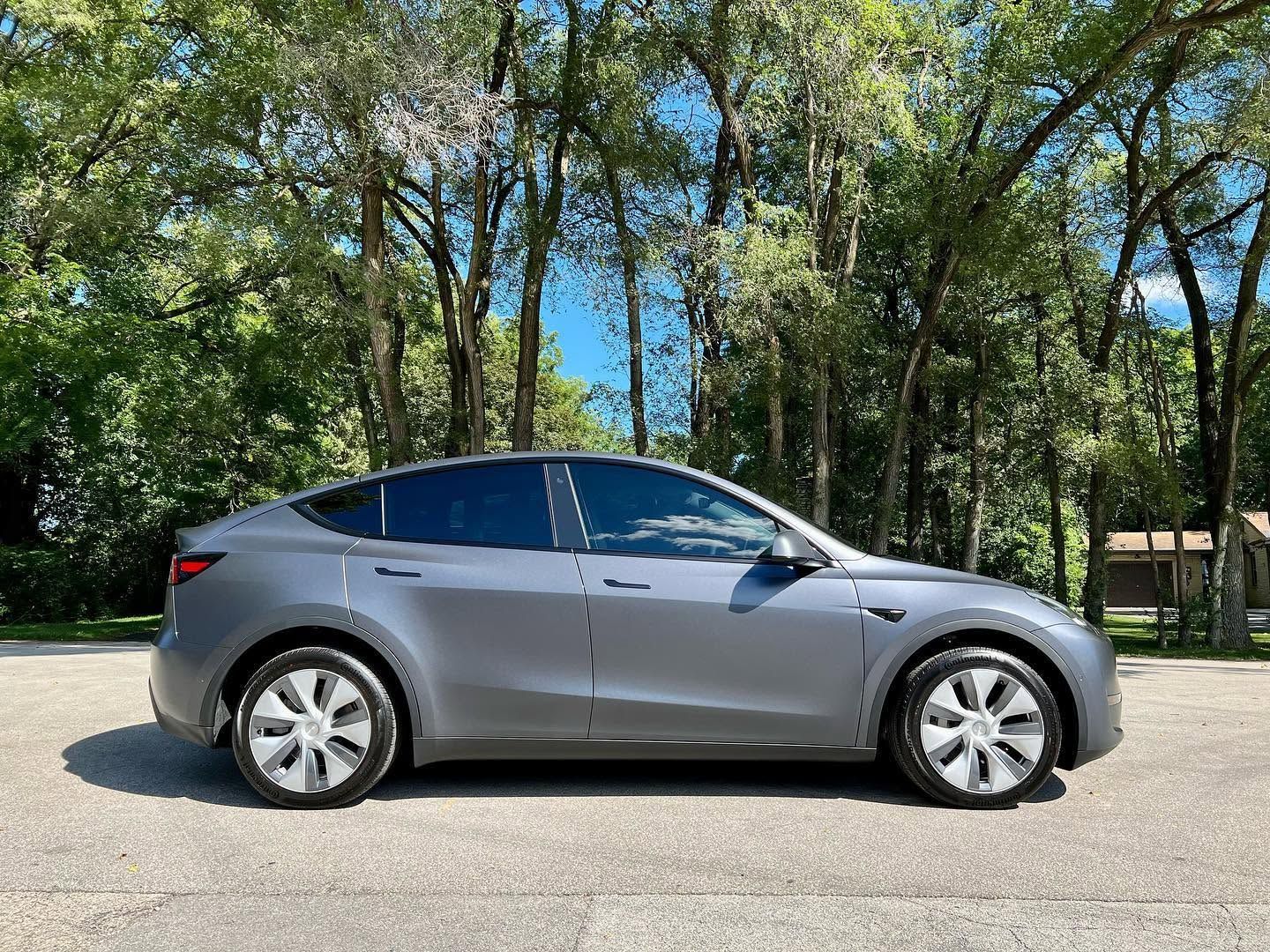 Silver Tesla sedan parked on a road with trees in the background